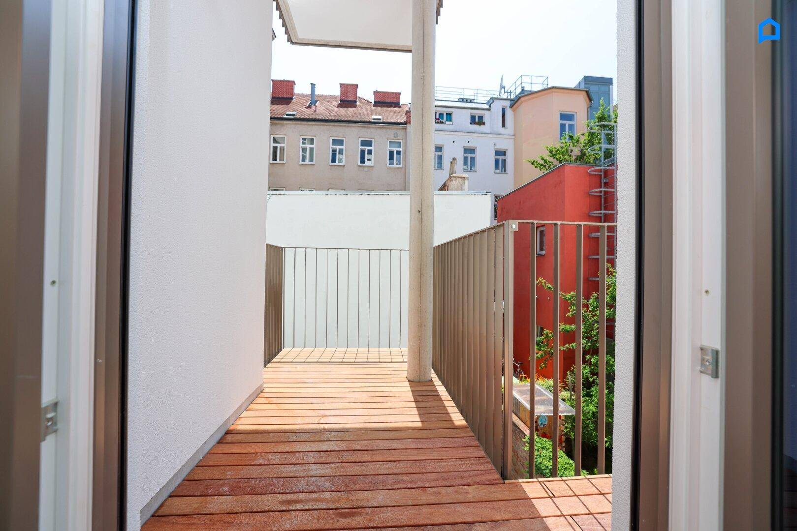 Heller Holzbalkon mit modernem Metallgeländer und Blick auf umliegende Gebäude.