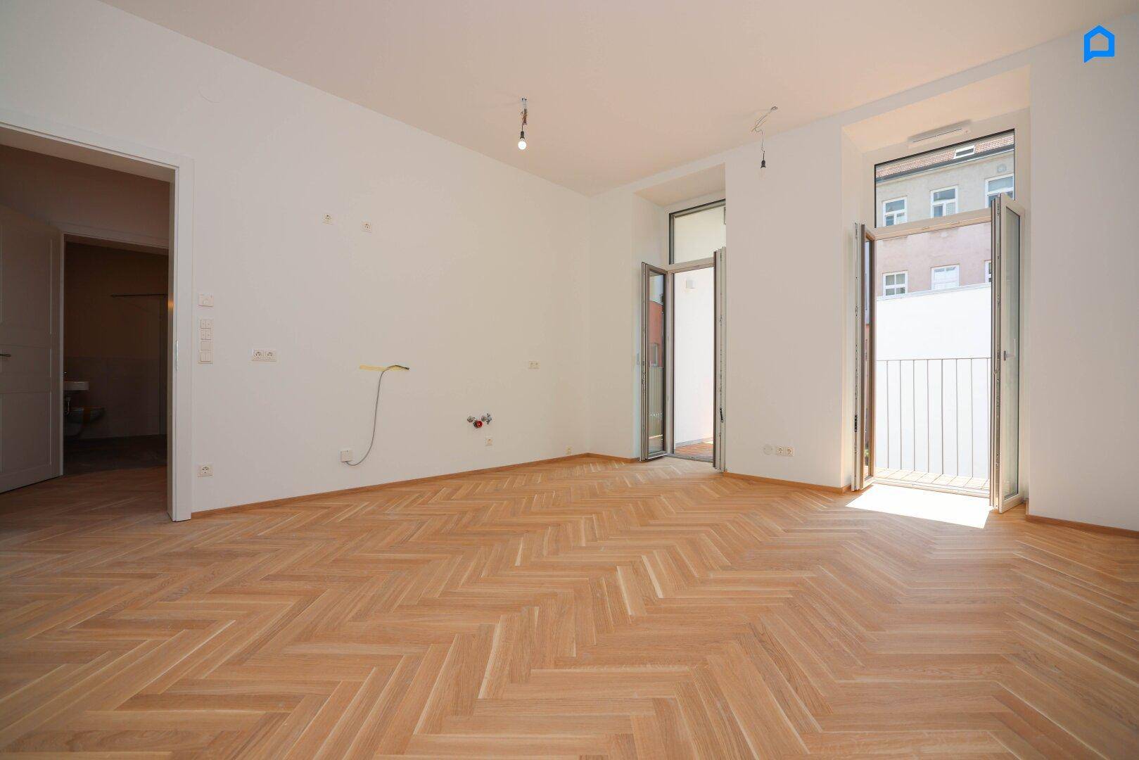 Geräumiges Zimmer mit Fischgrätparkett und Zugang zu einem französischen Balkon.