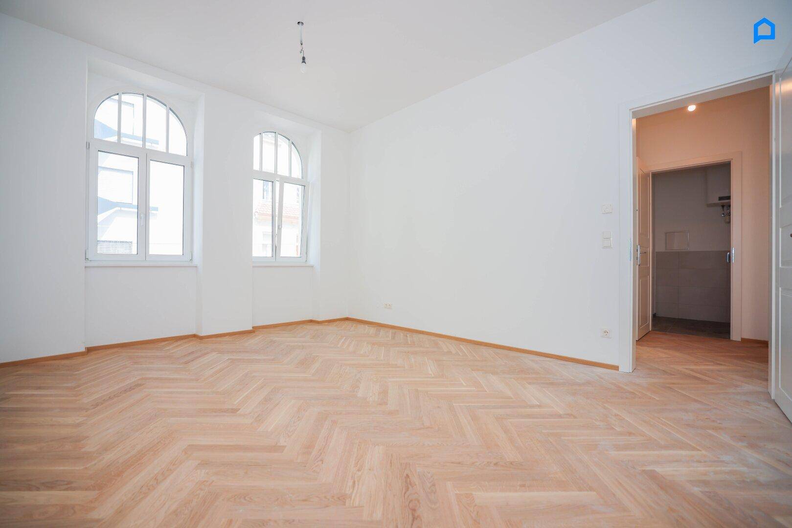 Helles Zimmer mit Fischgrätparkett und eleganten Rundbogenfenstern, ideal für Wohnzwecke.