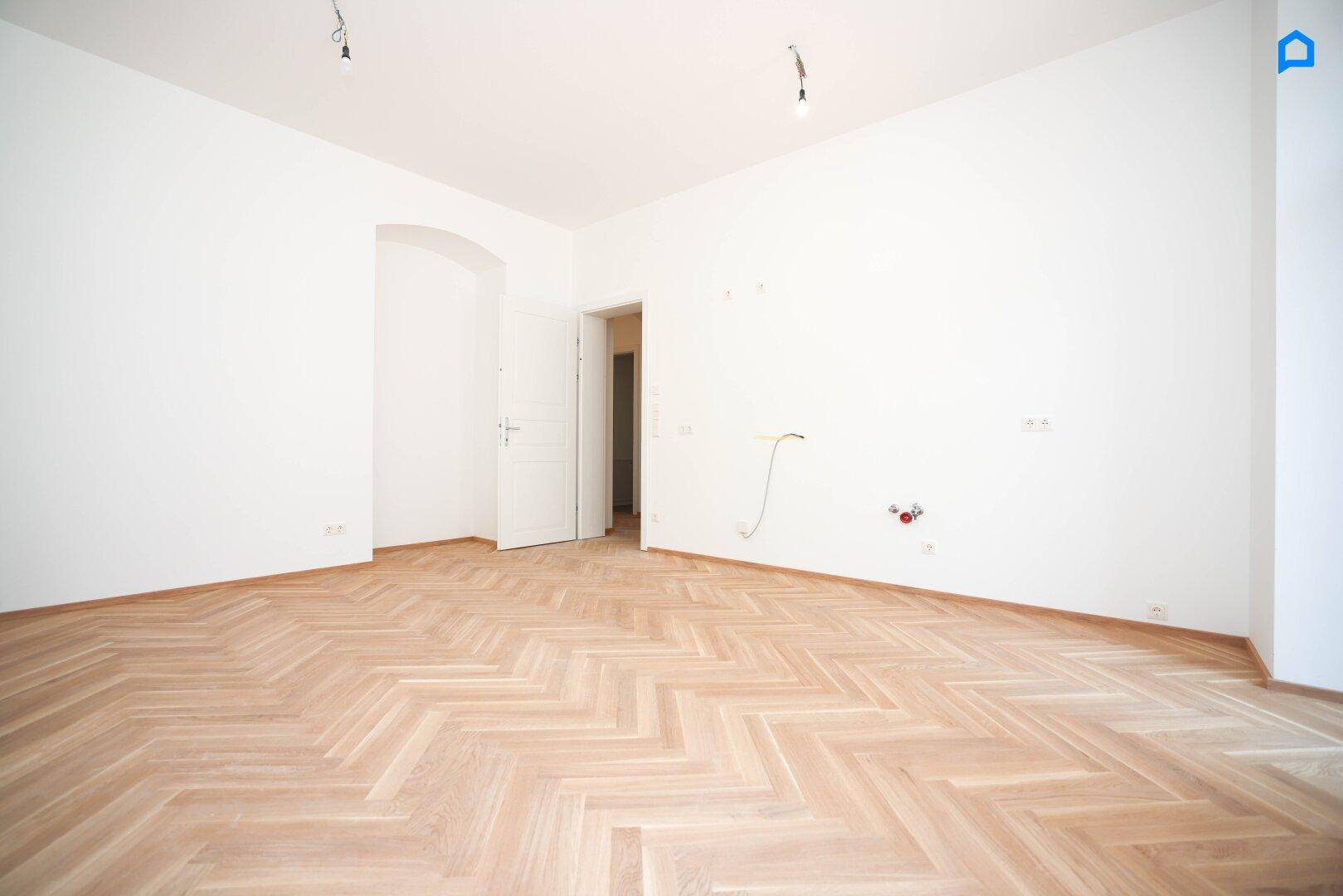 Leeres Zimmer mit Fischgrätparkett und weiß gestrichenen Wänden, bereit zum Einzug.