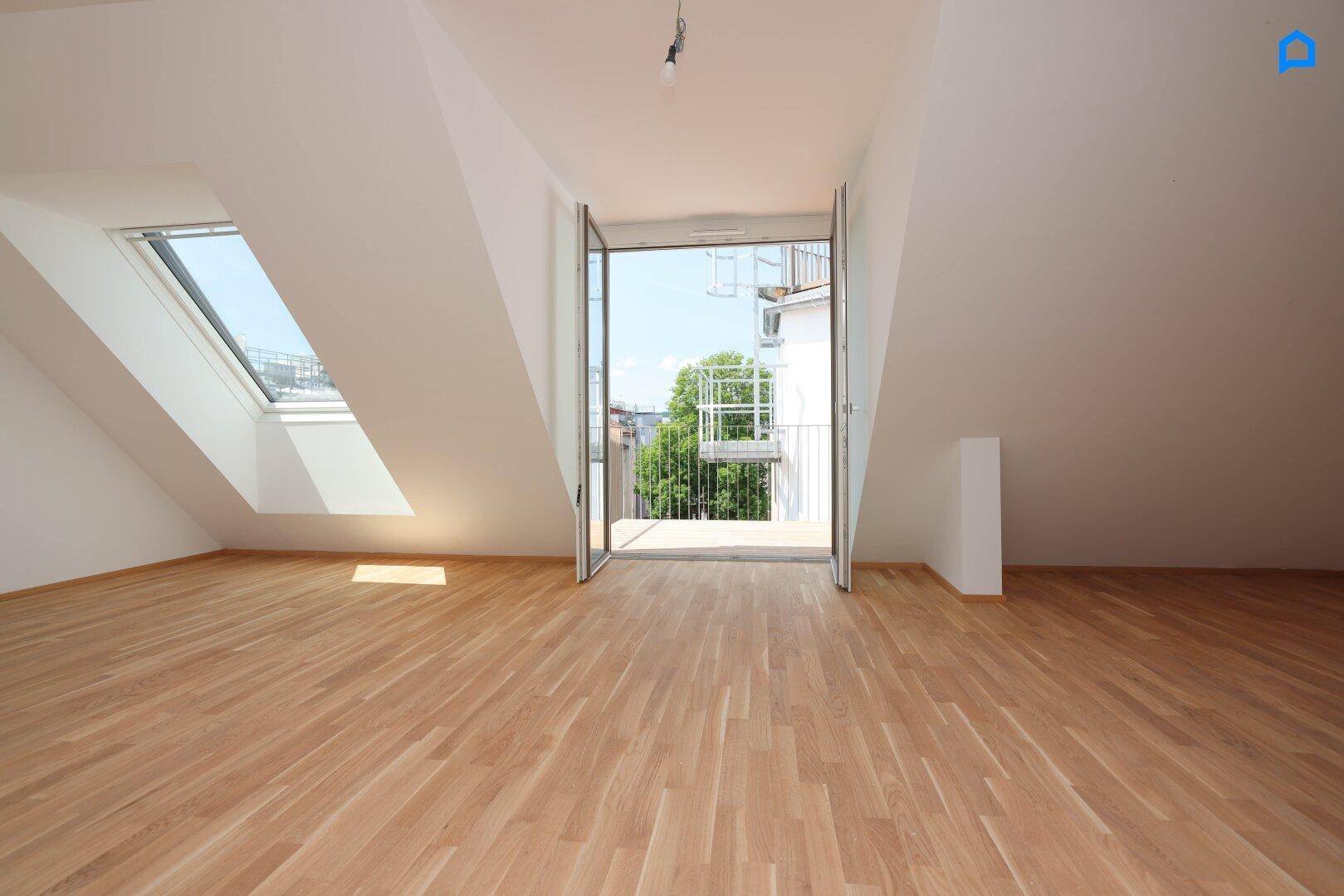Helles Dachgeschosszimmer mit Holzboden, Dachfenster und Zugang zu einem Balkon.