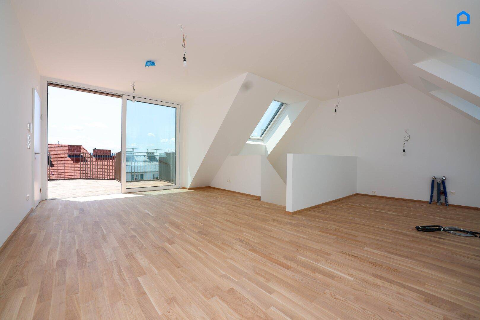 Geräumiger Dachbodenraum mit Holzboden, großen Fenstern und Zugang zu einer Dachterrasse.