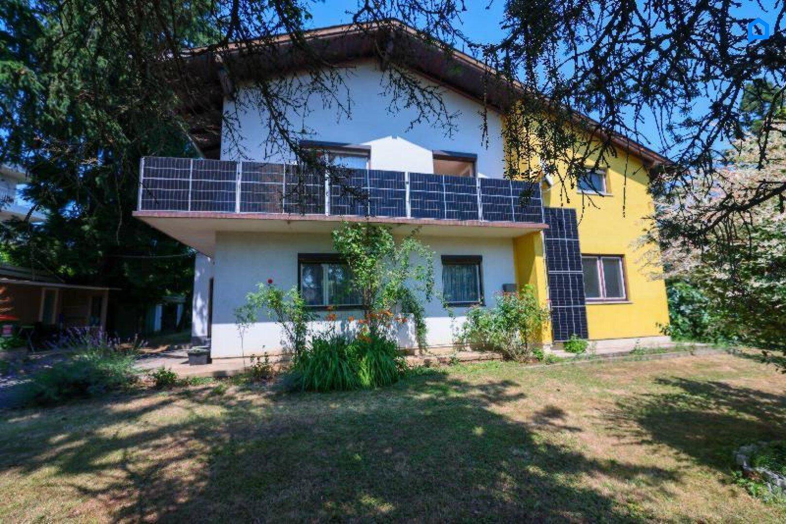 Rückansicht des Hauses mit Balkon, Solarpaneelen und einem grünen Gartenbereich.