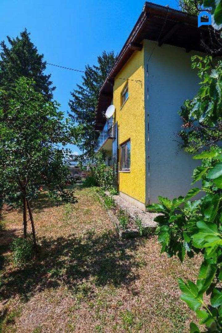 Seitenansicht des Hauses mit gelber Fassade und einem naturbelassenen Gartenbereich.