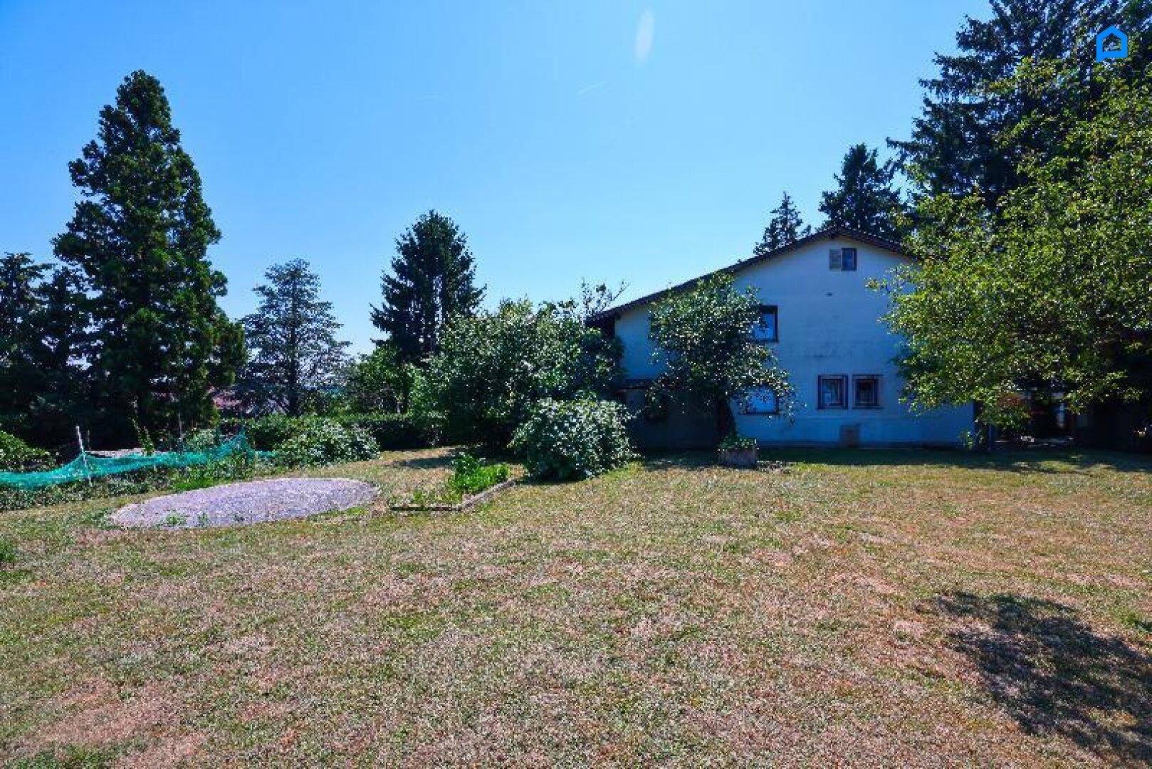 Hinterer Gartenbereich mit Rasen, Bäumen und dem Haus im Hintergrund an einem sonnigen Tag.