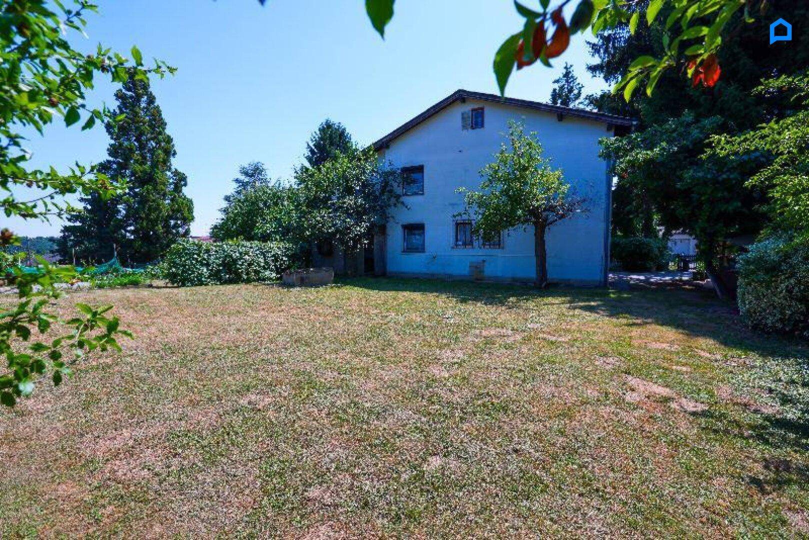 Großer Garten mit Rasen und Bäumen, der das Haus umgibt, unter klarem blauem Himmel.