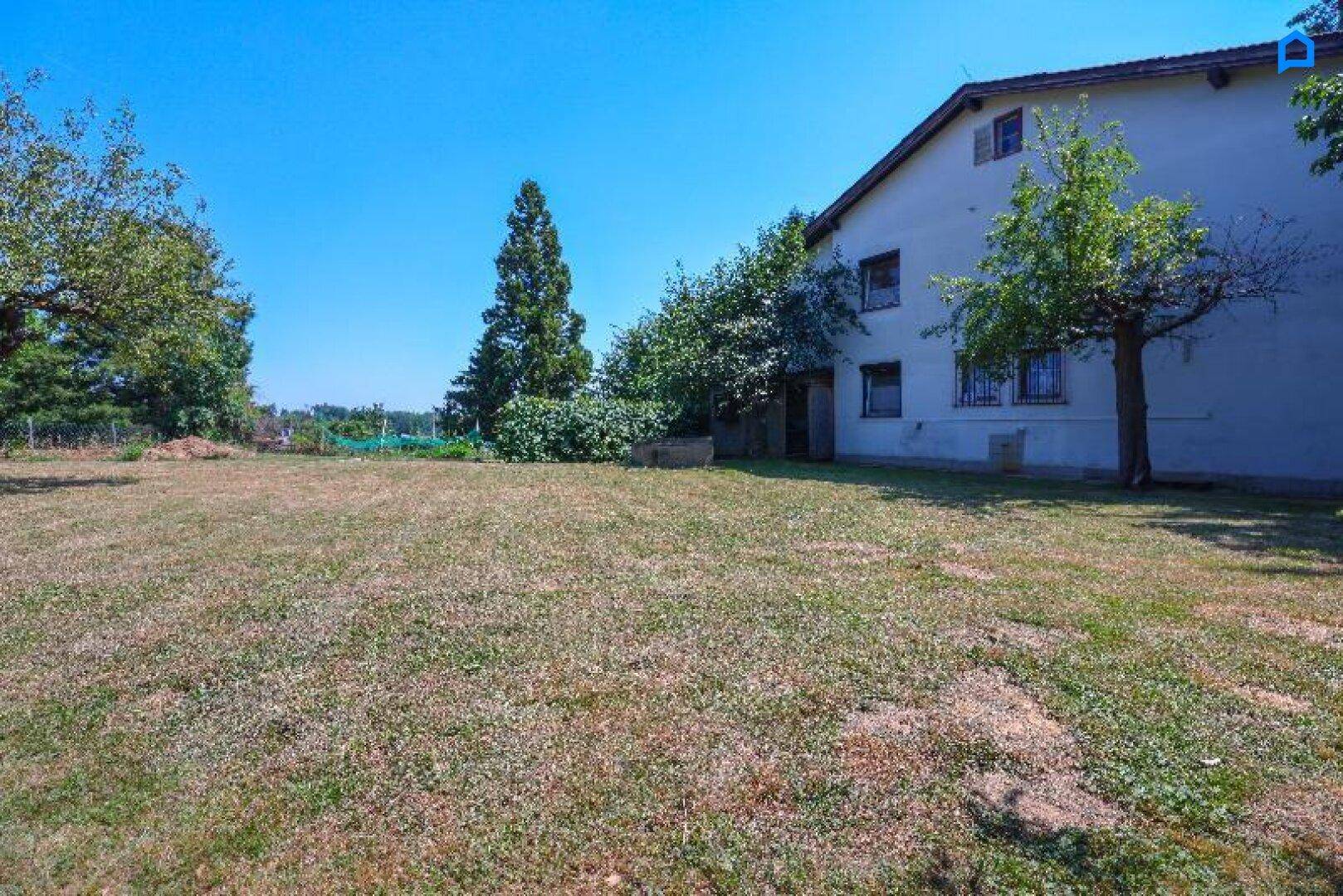 Großer Garten mit Rasenfläche und Bäumen, der zum Haus führt, unter blauem Himmel.