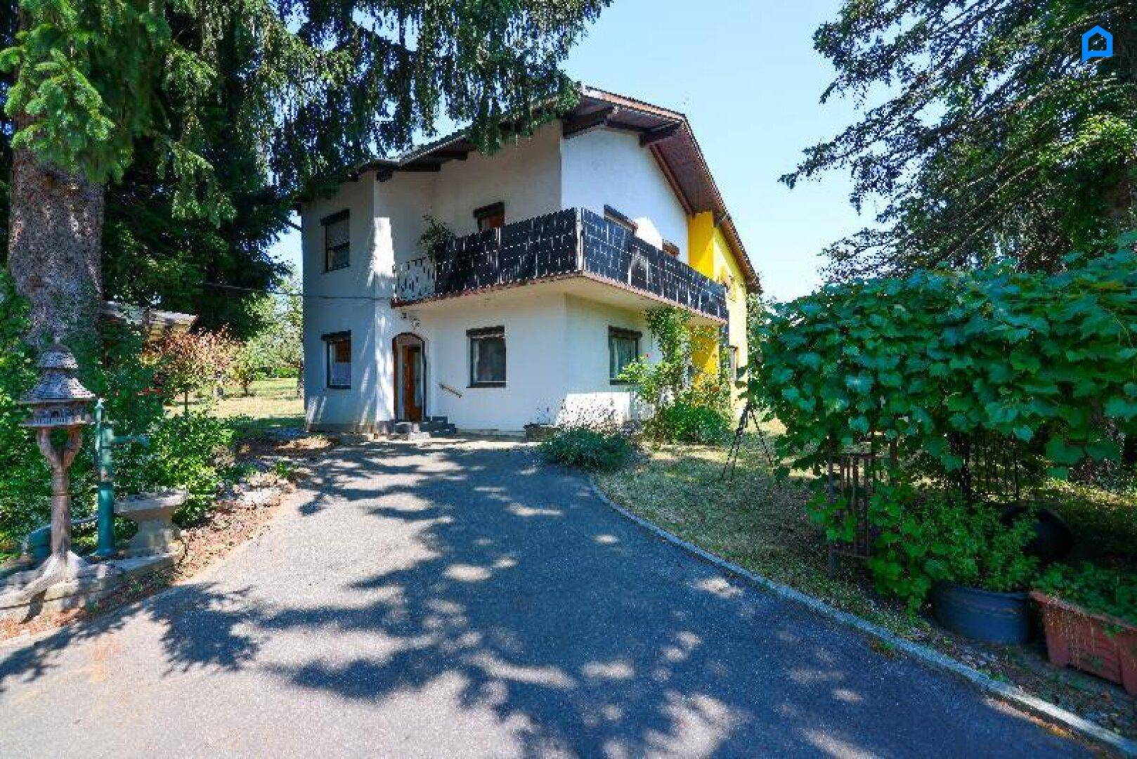 Einfamilienhaus mit weißer und gelber Fassade, umgeben von Bäumen und einem gepflasterten Weg.