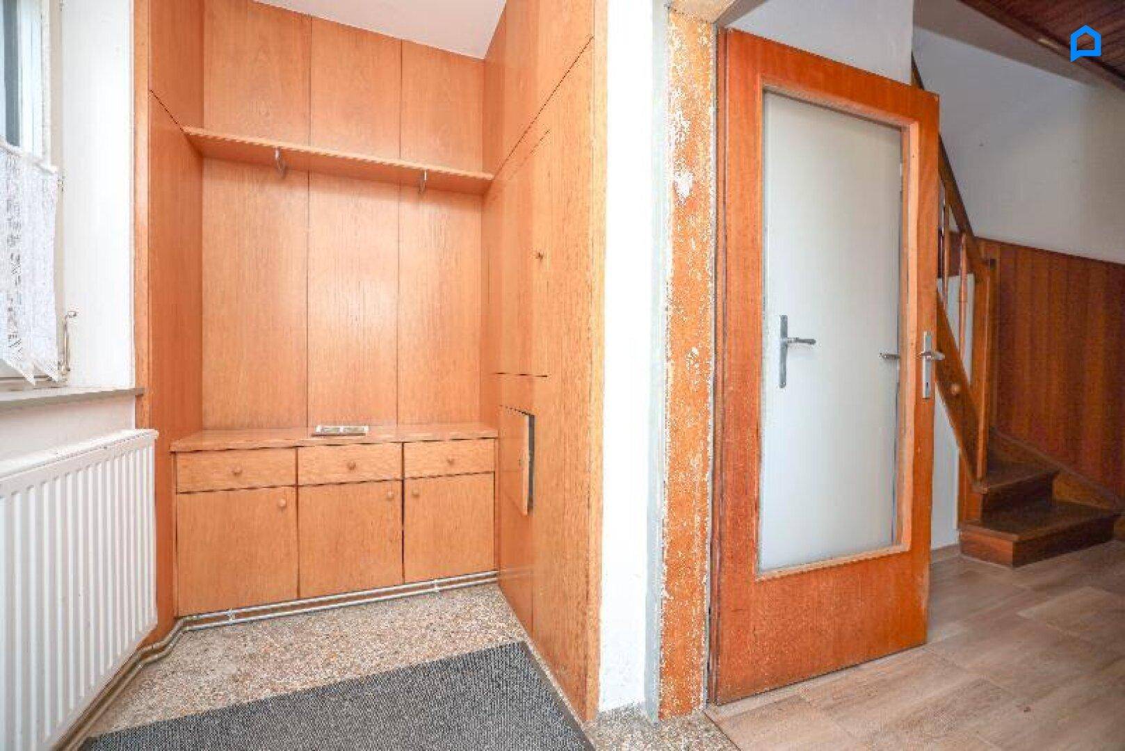 Eingangsbereich mit Holzvertäfelung, Einbauschränken und einer Treppe zum Obergeschoss.