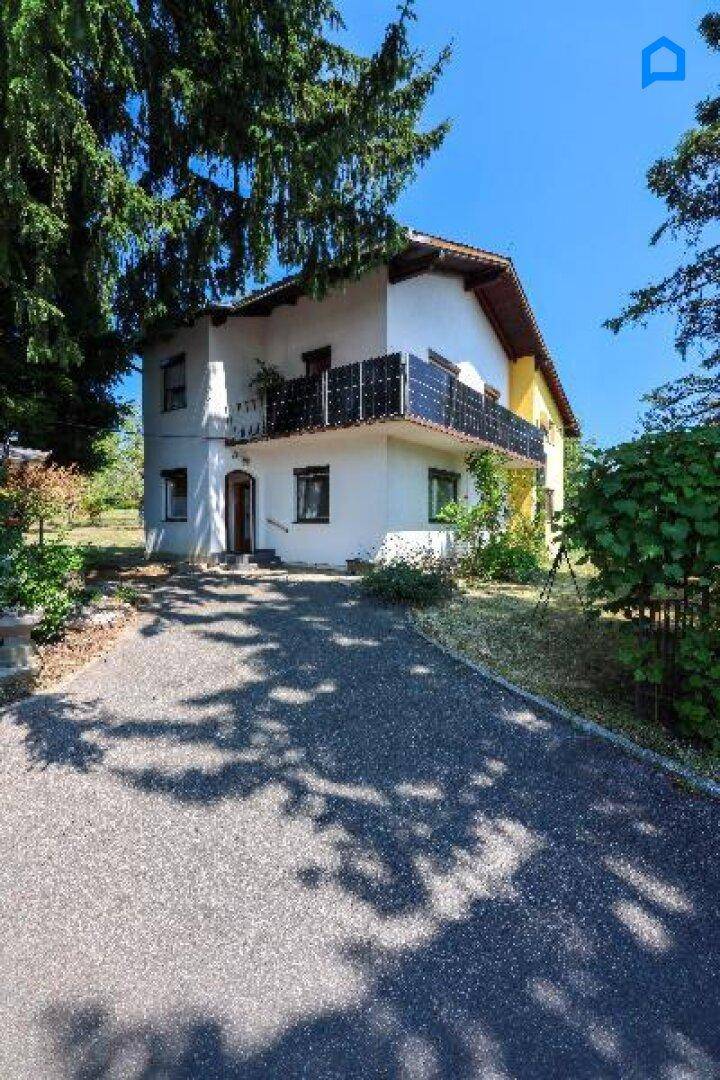 Einfamilienhaus mit weißer und gelber Fassade, umgeben von Bäumen und einem gepflasterten Weg.