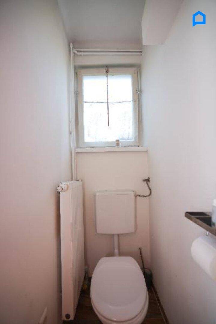 Kleines Gäste-WC mit Fenster, Toilette und Heizkörper in schlichtem Design.