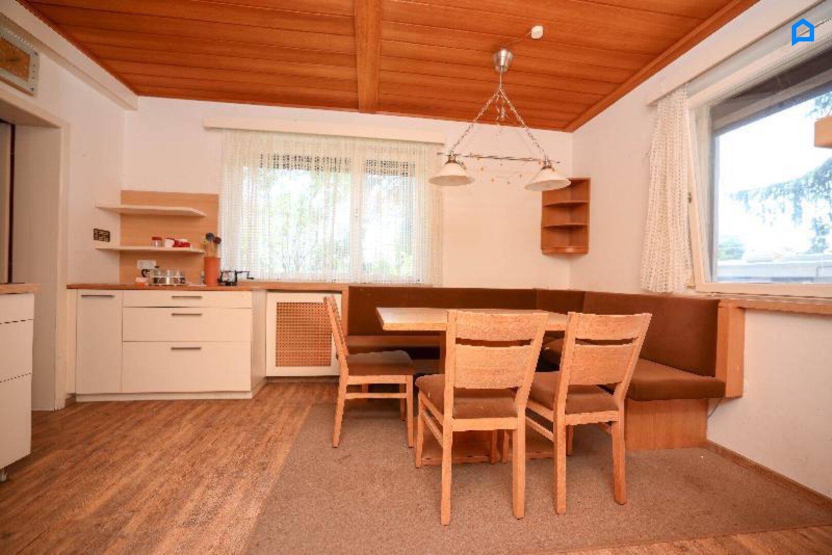Gemütliche Wohnküche mit Holztisch, Eckbank und Holzdecke, ideal für Familienmahlzeiten.
