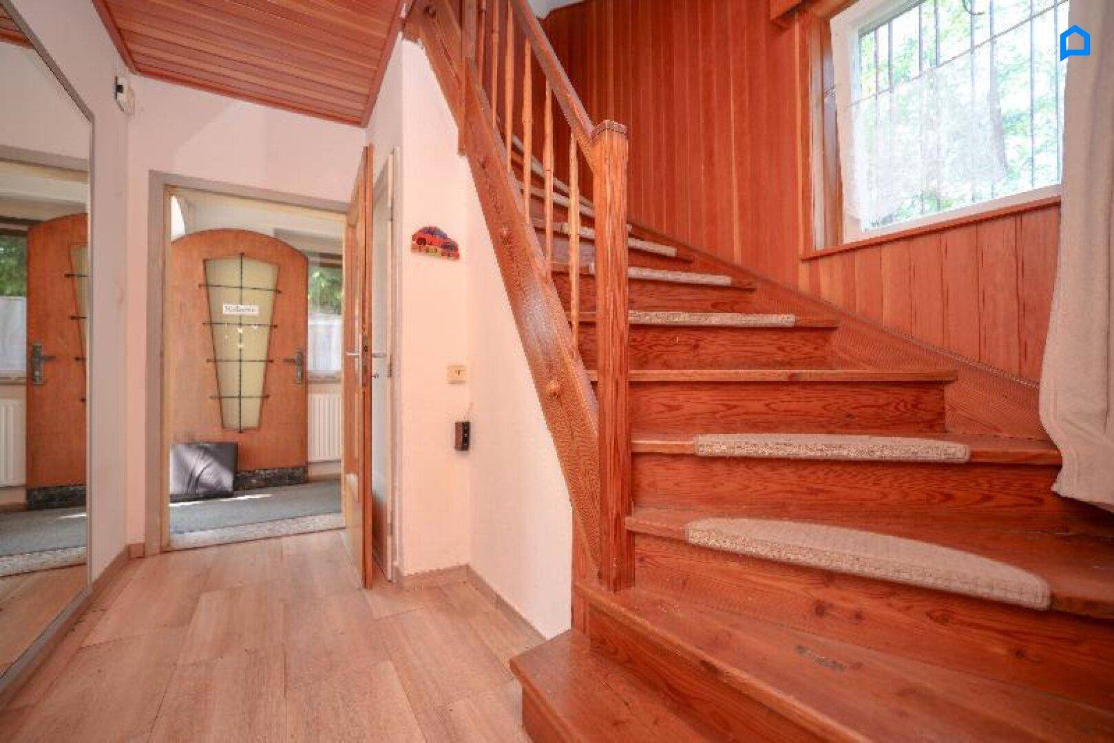 Heller Flur mit Holztreppe, Holzvertäfelung und Zugang zu weiteren Räumen.