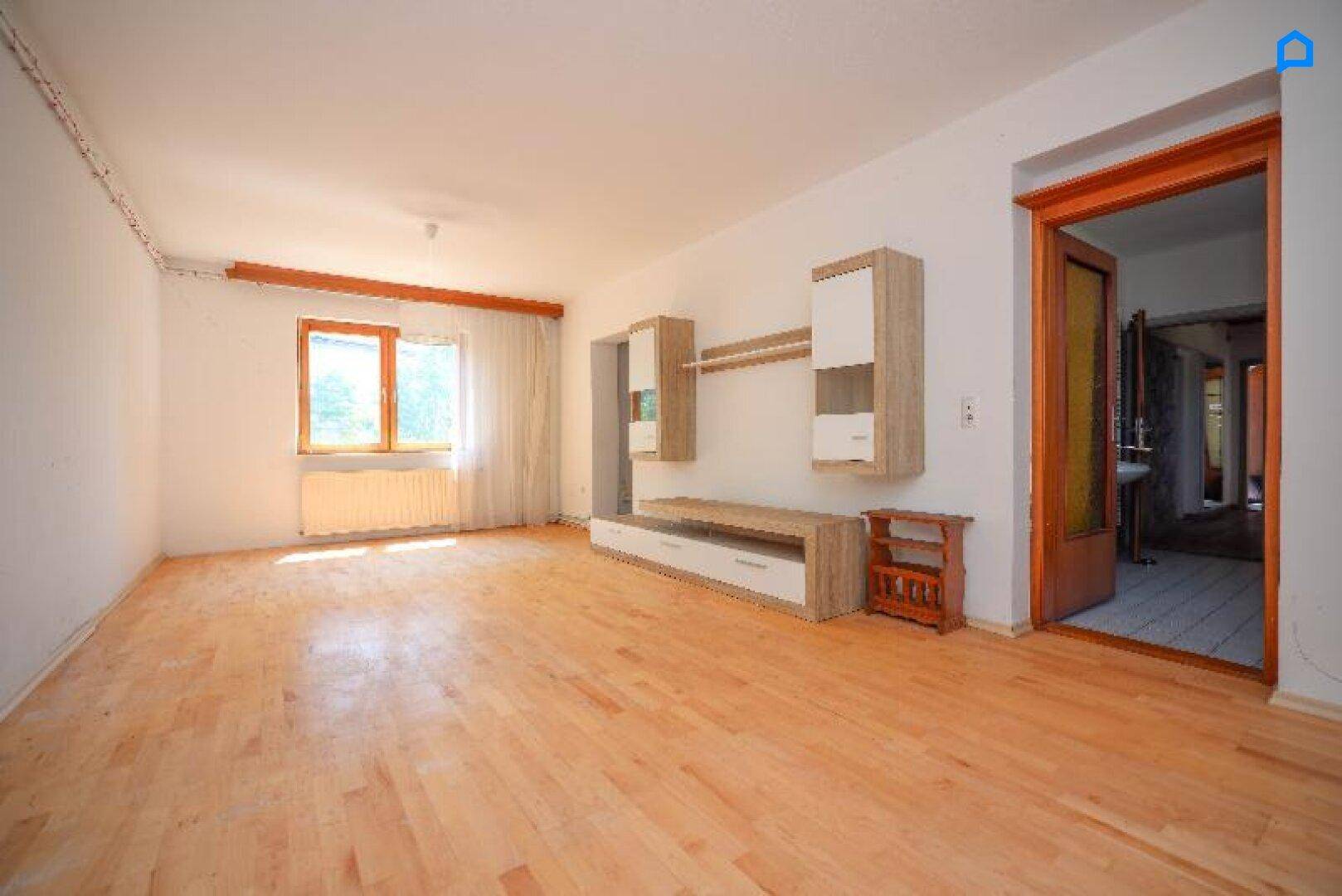 Geräumiges Wohnzimmer mit Holzboden, Fenster und modernen Wandregalen.