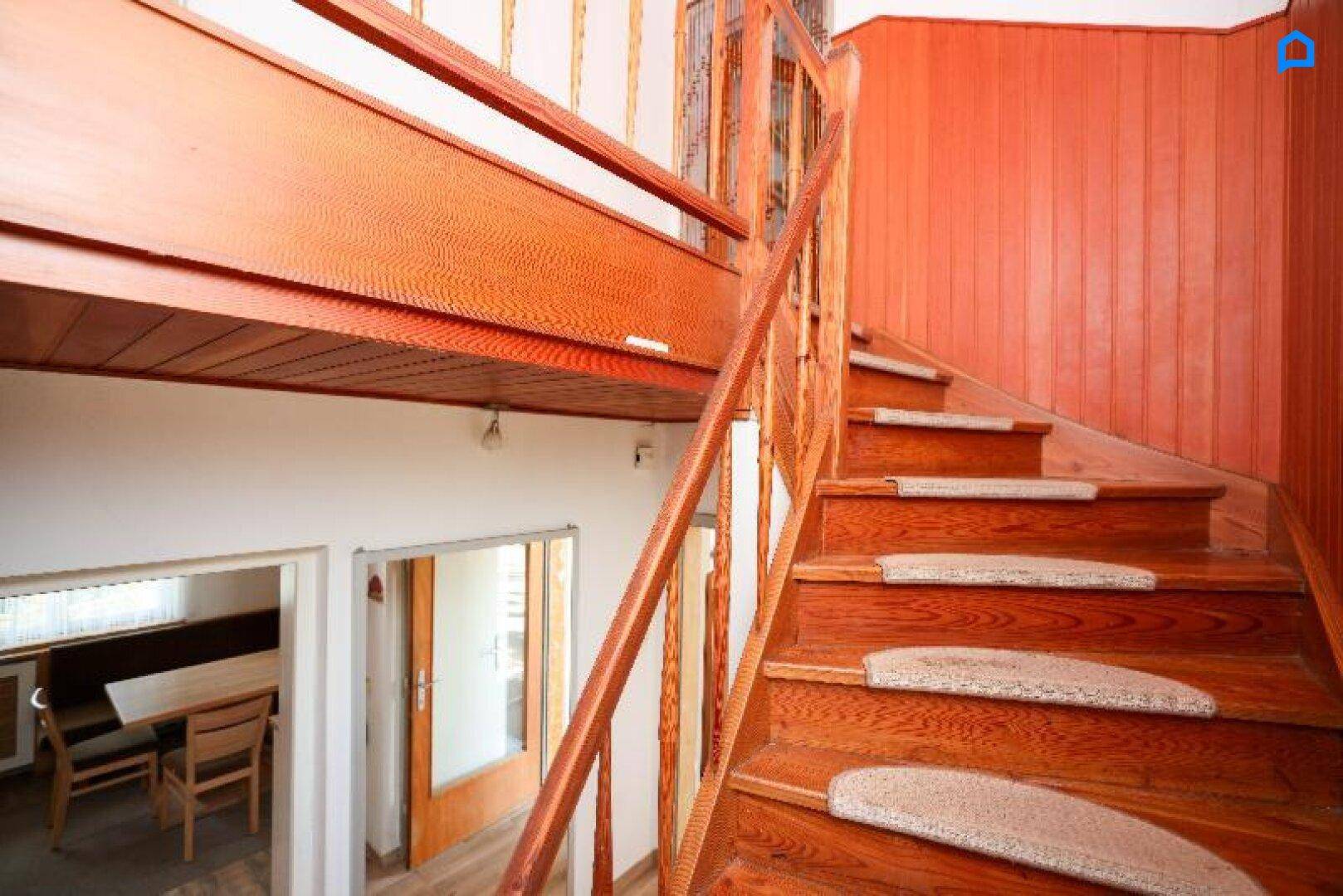 Holztreppe mit Teppichläufern führt in das obere Stockwerk, mit Blick auf den Essbereich.