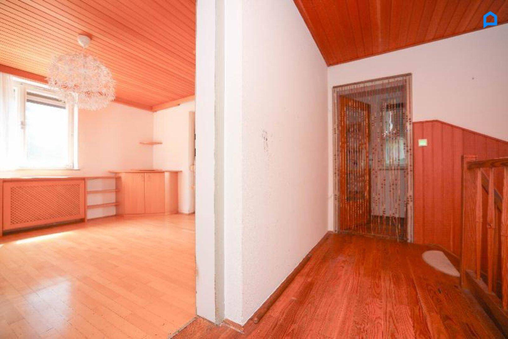 Heller Flur mit Holzboden und Holzdecke, führt zu einem angrenzenden Zimmer.