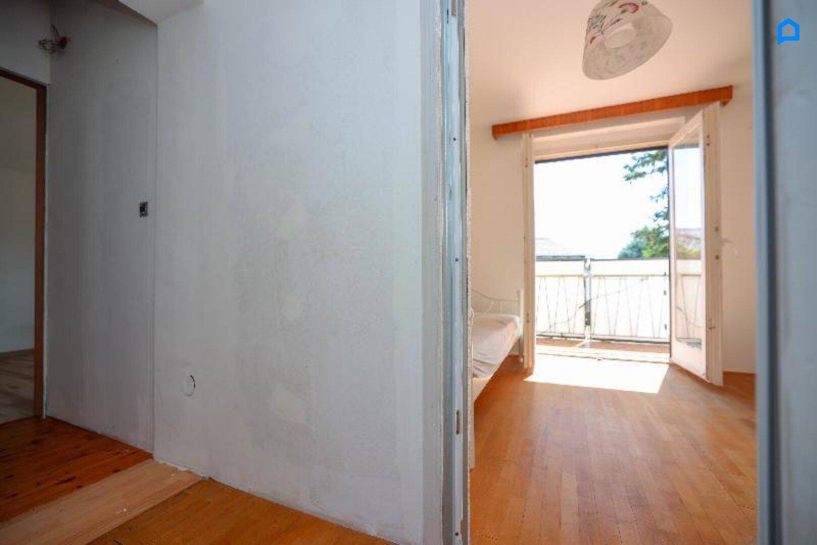 Helles Schlafzimmer mit Holzboden und direktem Zugang zu einem sonnigen Balkon.