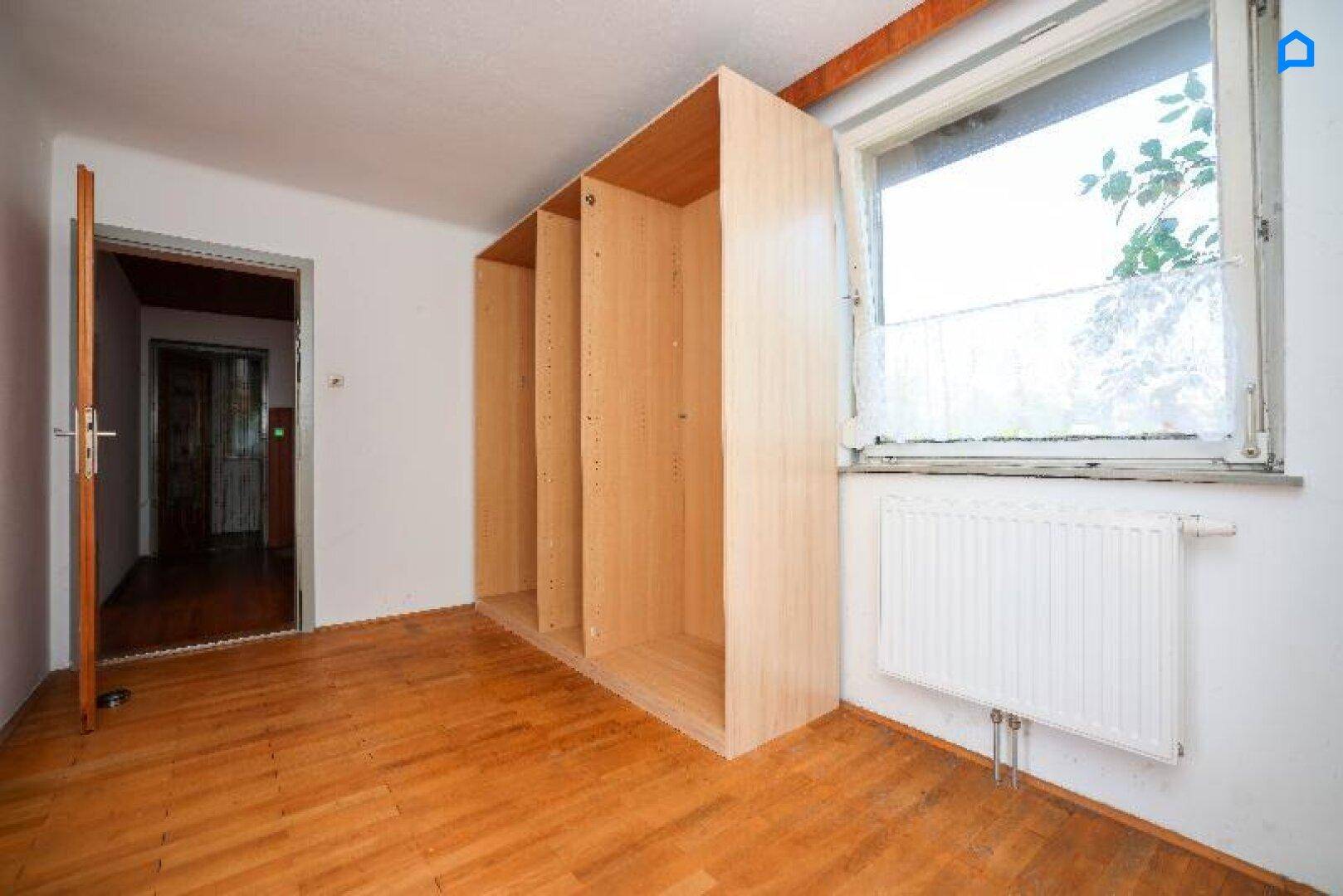 Innenraum mit Holzboden, eingebauten Regalen und Fenster, das Tageslicht hereinlässt.