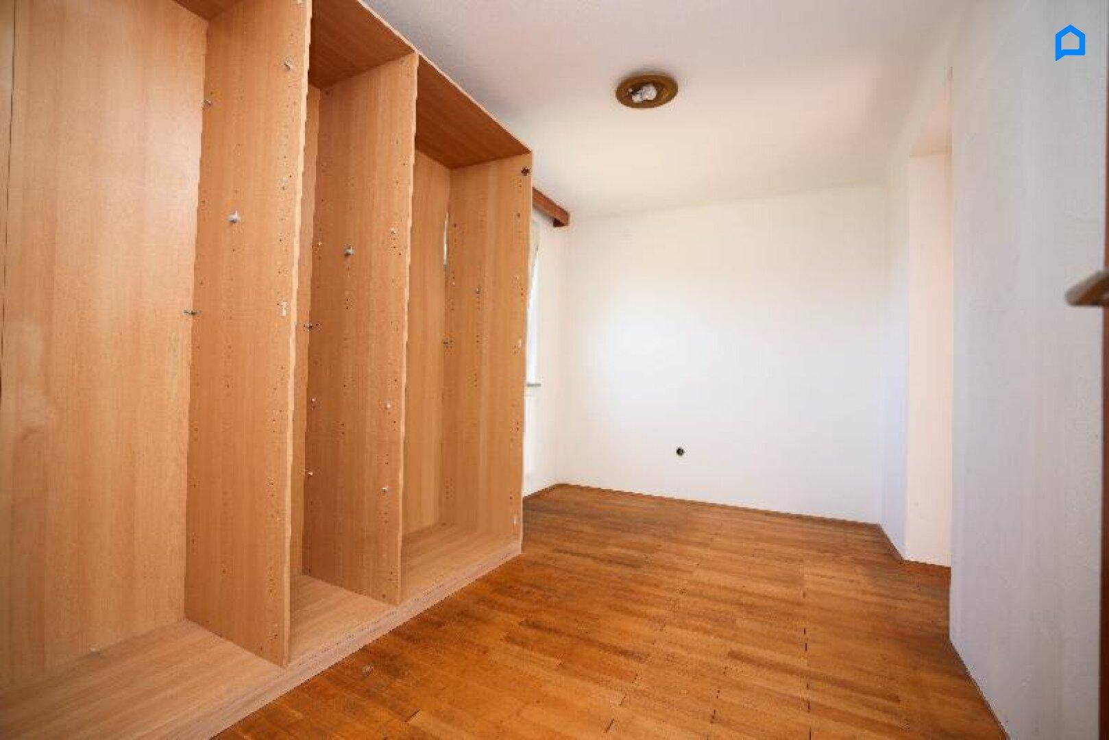 Heller Raum mit Holzboden und eingebauten Regalen, ideal als Ankleidezimmer oder Abstellraum.