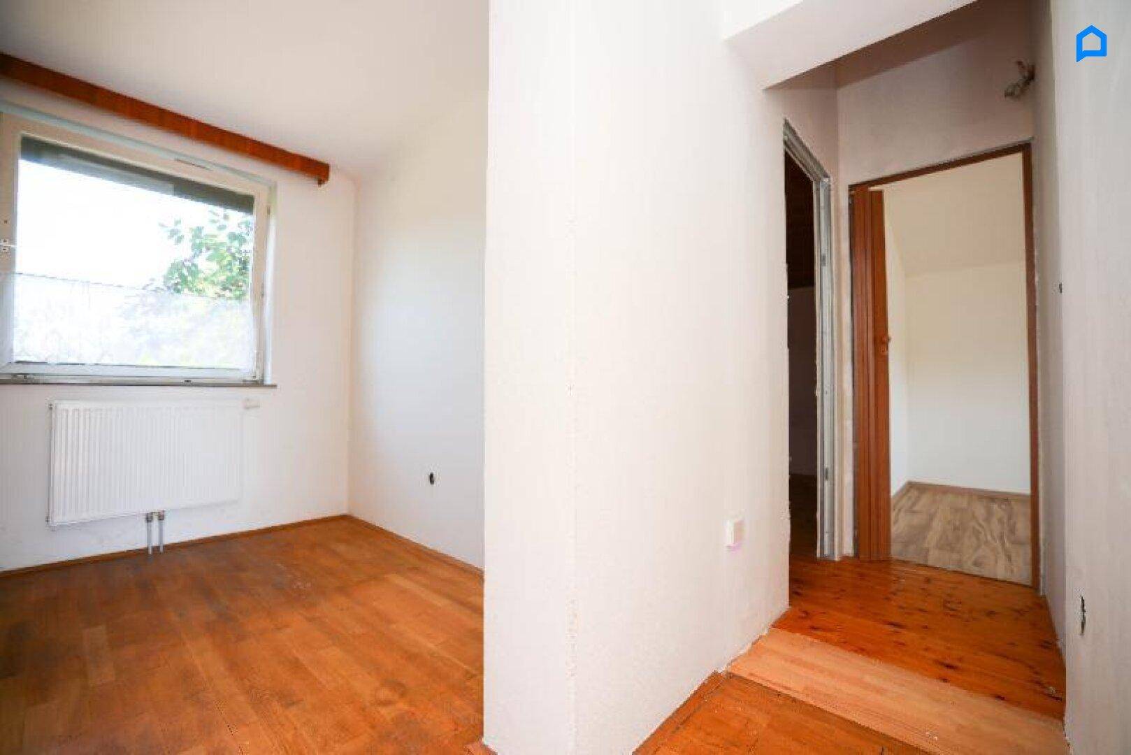 Kleiner Raum mit Holzboden und Fenster, der als Übergangsbereich oder Abstellraum dienen könnte.