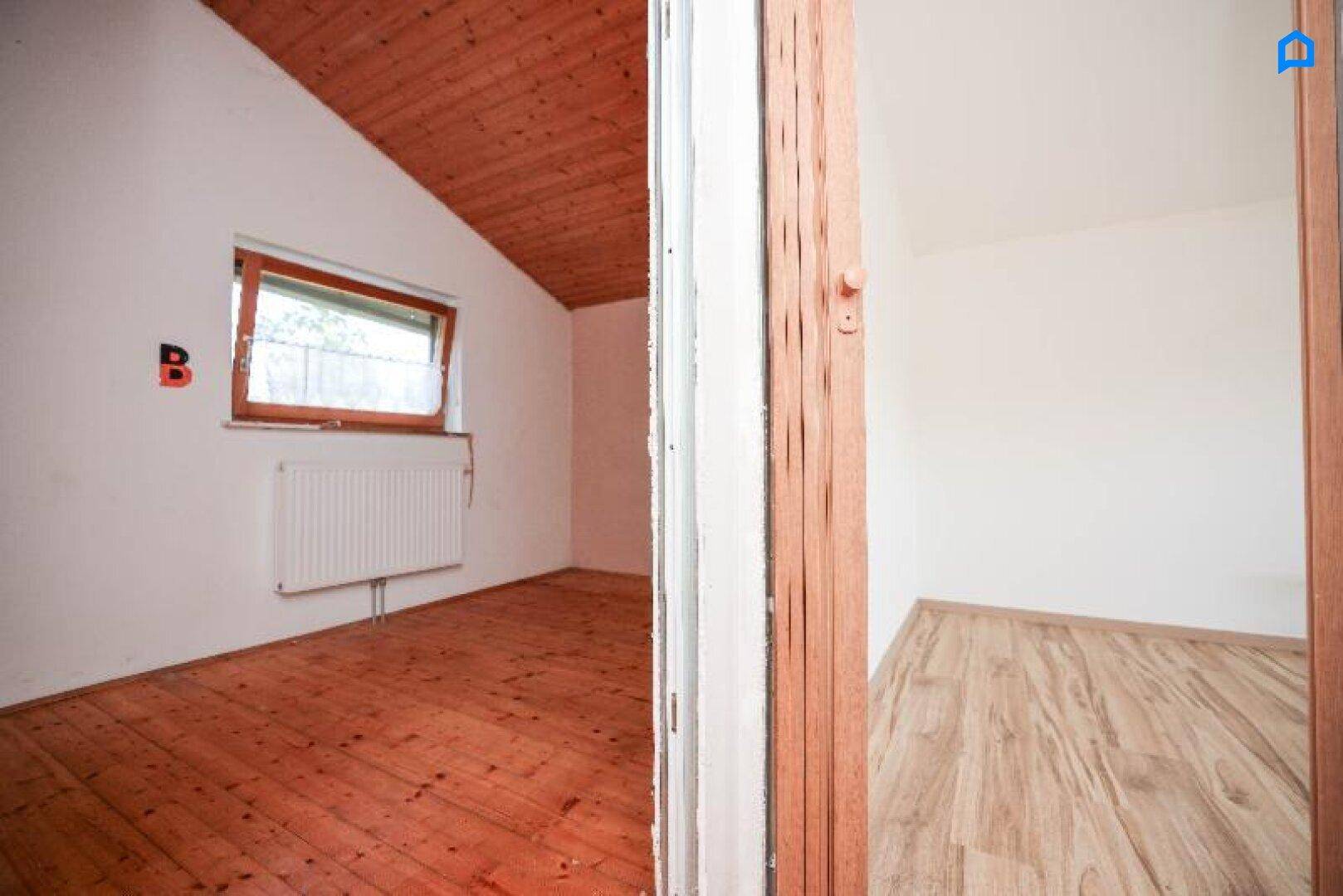 Gemütliches Schlafzimmer mit Holzboden, Dachschräge und Holzdecke, gut beleuchtet durch ein Fenster.