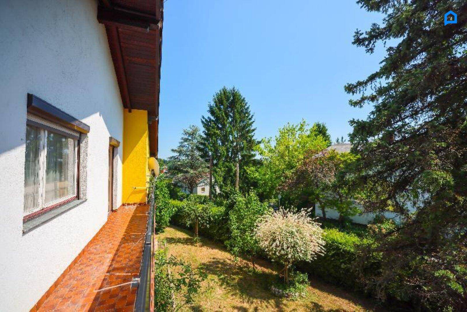 Blick vom Balkon auf den gepflegten Garten mit Hecken und verschiedenen Bäumen.