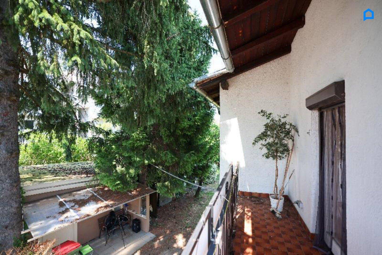 Sonniger Balkon mit Terrakottafliesen und schmiedeeisernem Geländer, umgeben von Bäumen.