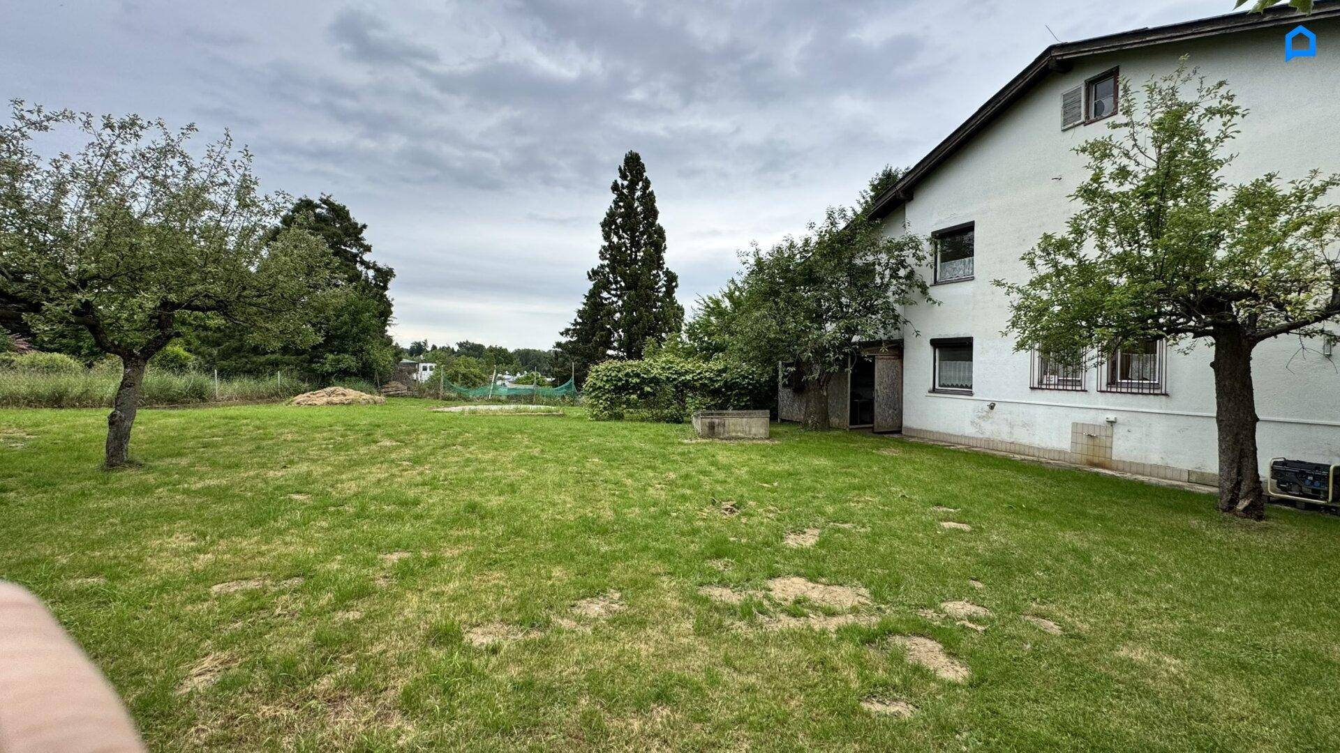 Weitläufiger Garten mit Rasenfläche und Bäumen, angrenzend an die Hausfassade.