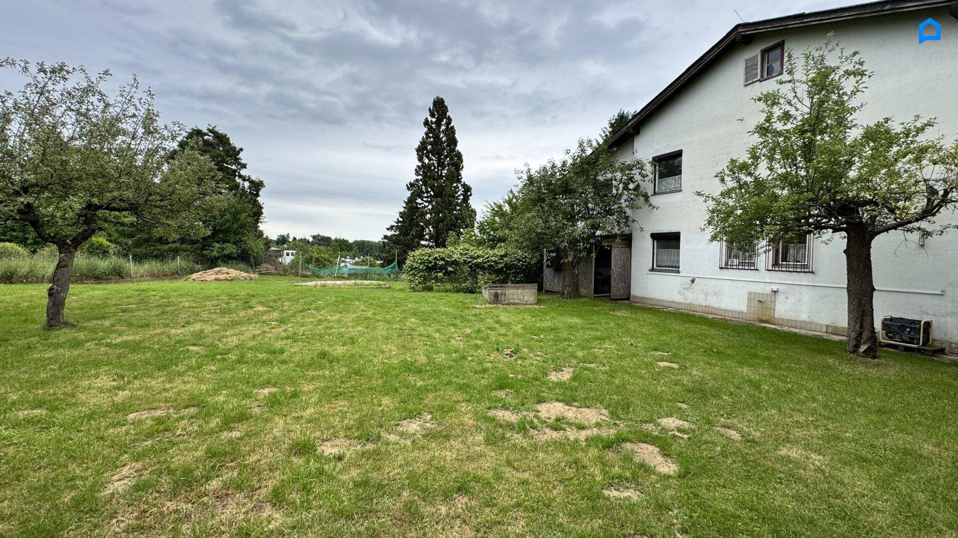Großer, gepflegter Garten mit Rasen und Obstbäumen neben dem Wohnhaus an einem bewölkten Tag.