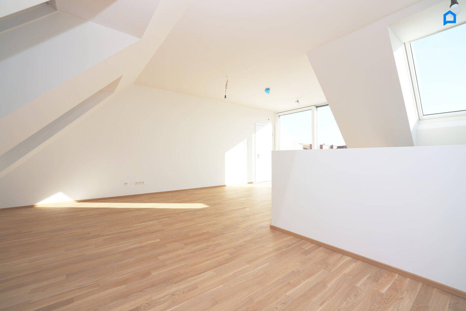 Heller Dachgeschossraum mit Holzboden und schrägen Wänden, durchflutet von natürlichem Licht.