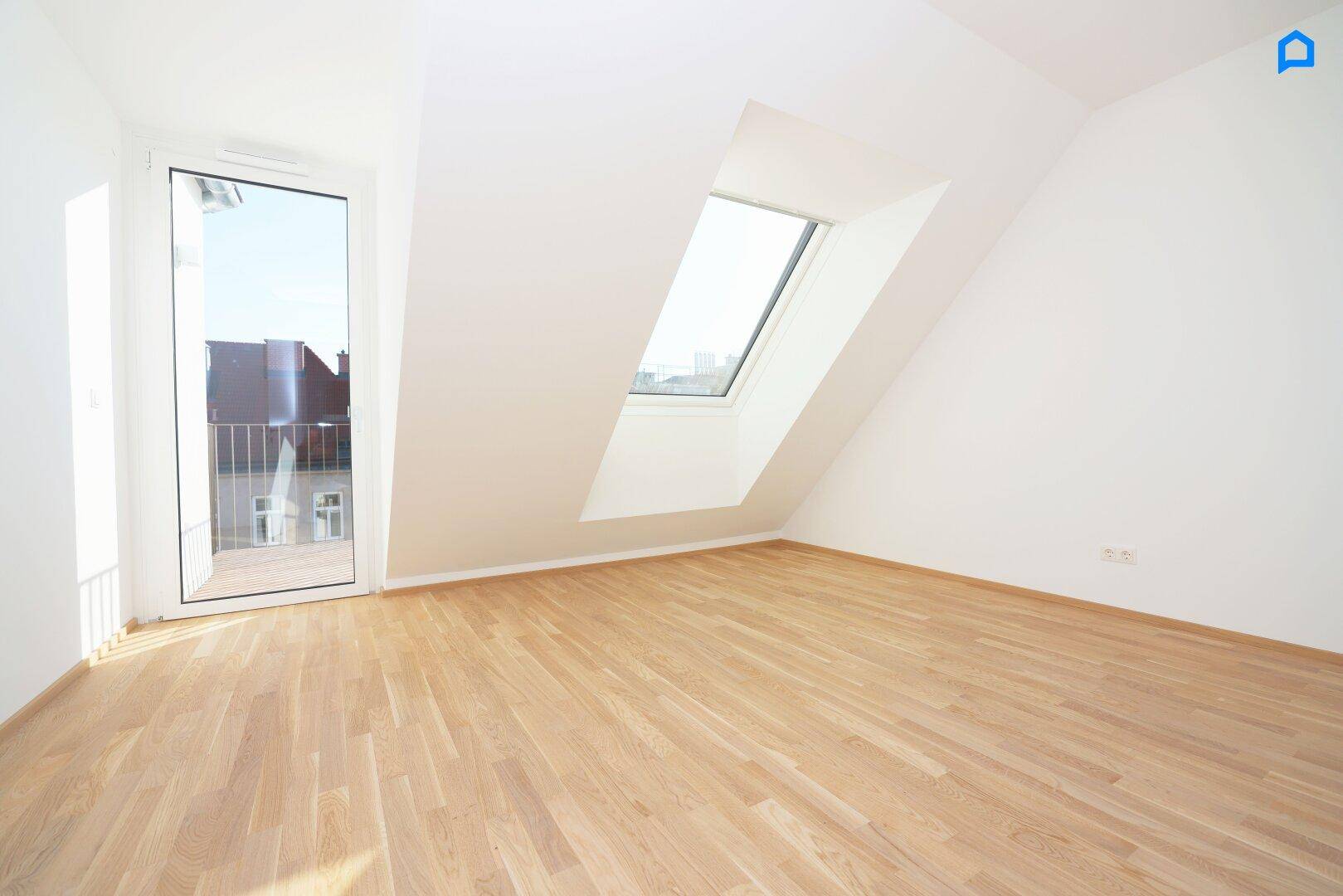 Helles Zimmer im Dachgeschoss mit Holzboden, Dachfenster und Zugang zu einem kleinen Balkon.