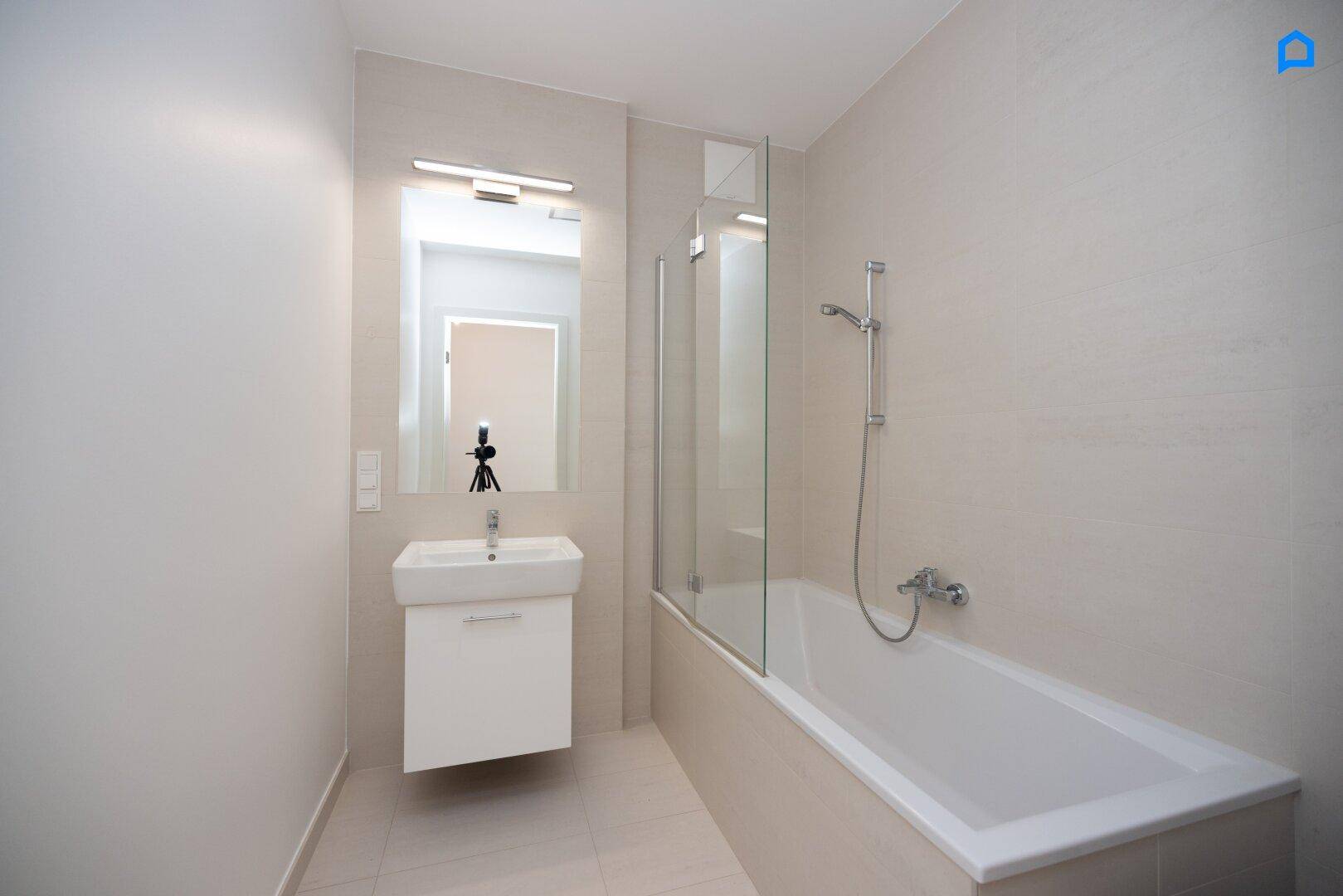Modernes Badezimmer mit Badewanne, Waschbecken und großem Spiegel, hell gefliest.