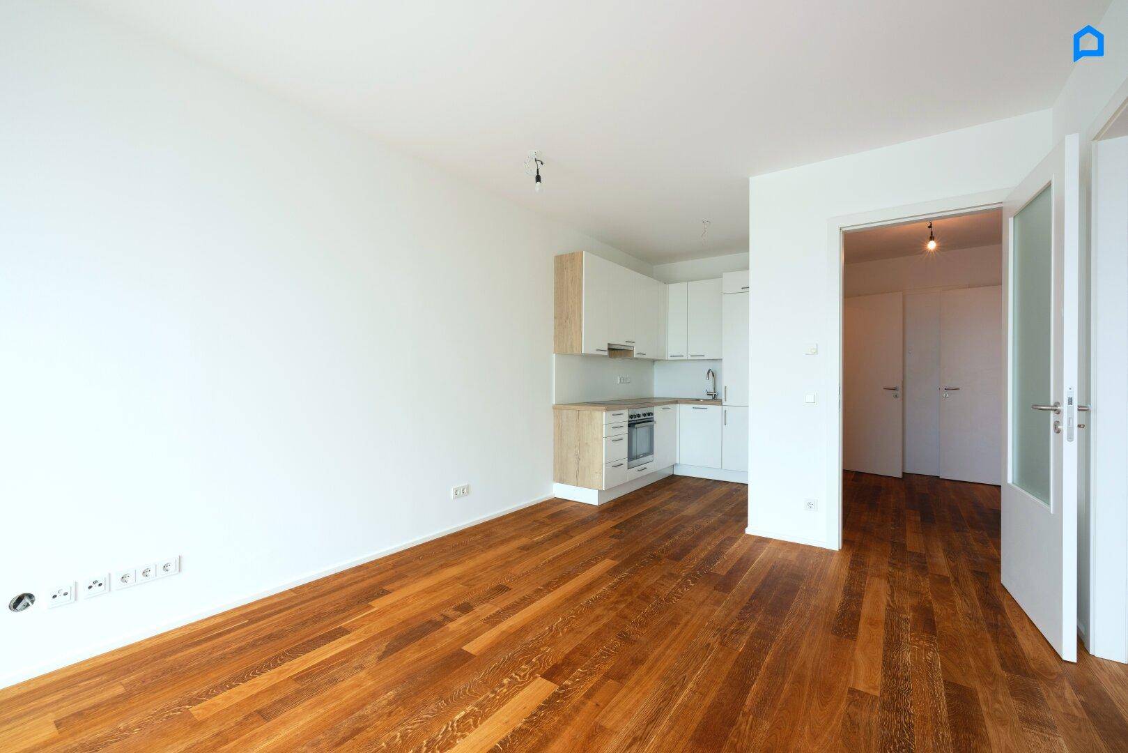 Heller Wohnbereich mit integrierter Küchenzeile und Holzboden, verbunden mit weiteren Räumen.