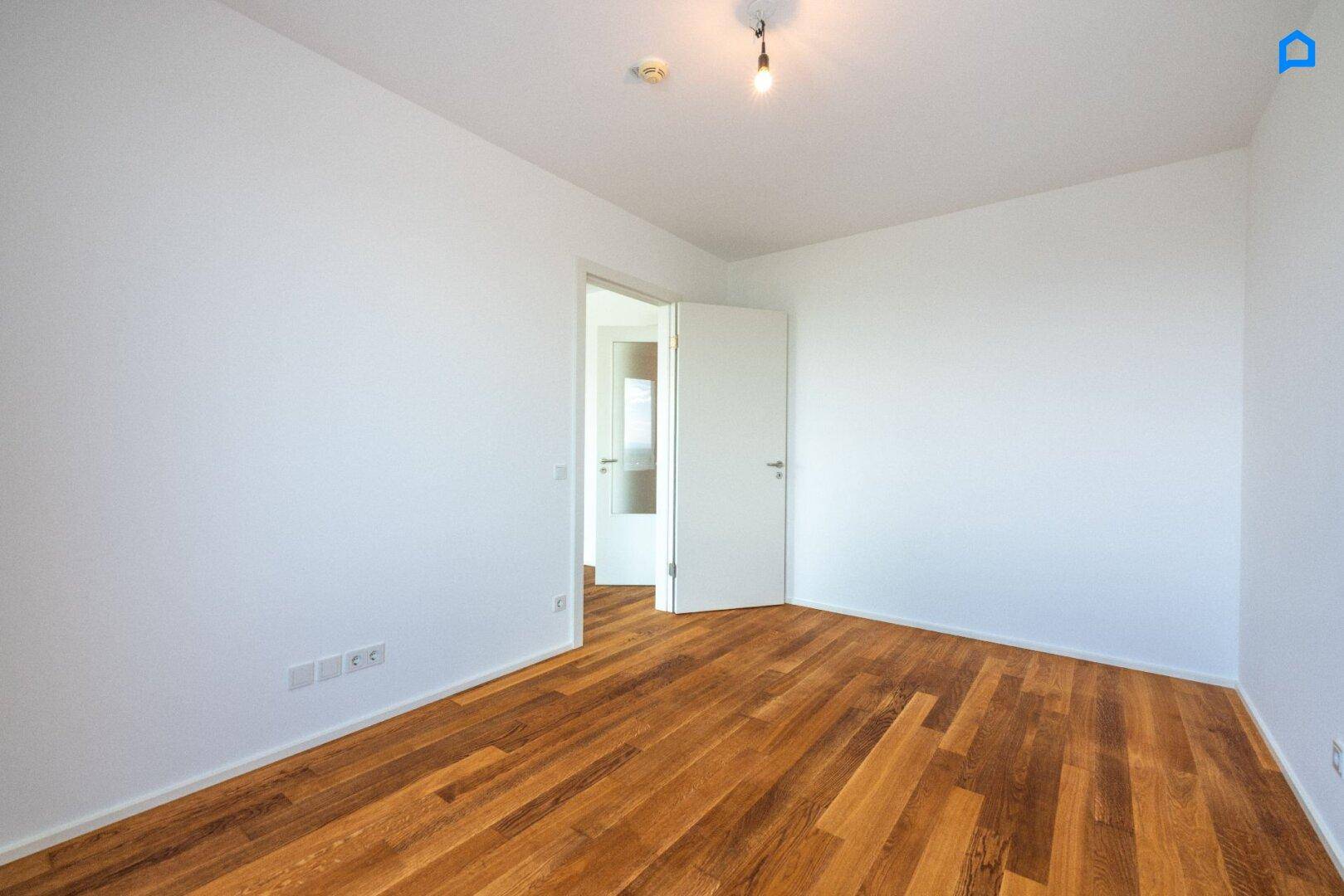 Leeres Zimmer mit Holzboden und weiß gestrichenen Wänden, bereit zur individuellen Gestaltung.