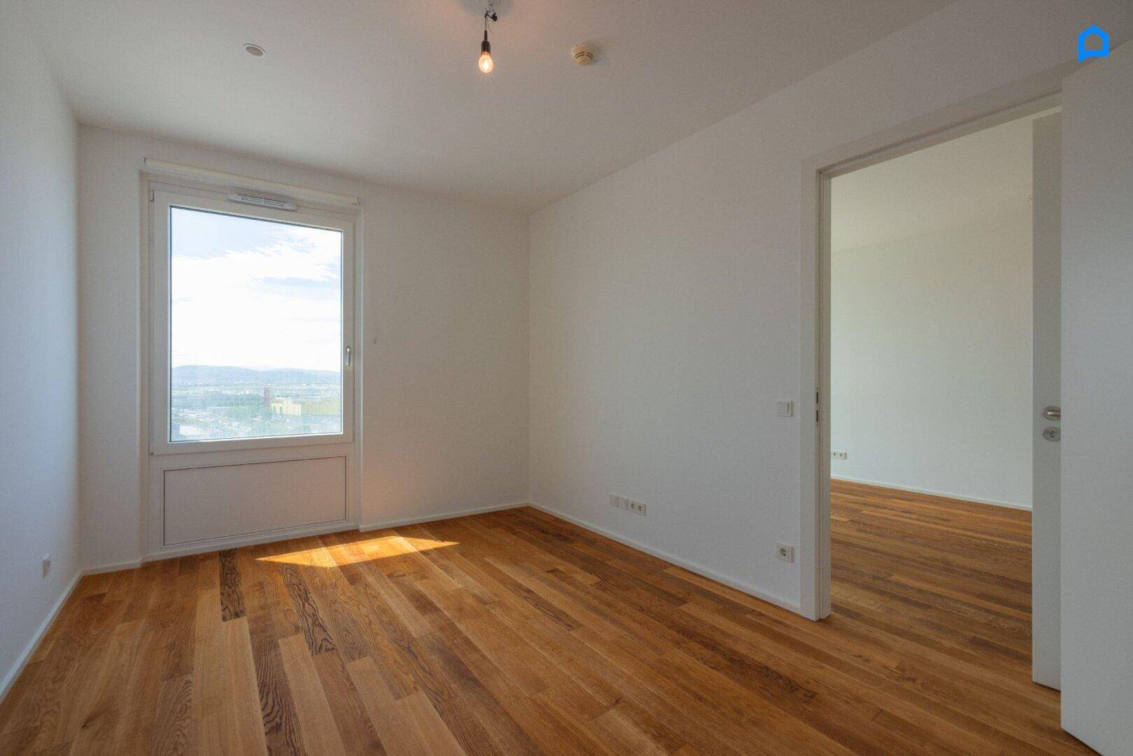 Helles Schlafzimmer mit Holzboden und einem großen Fenster, das einen weiten Ausblick bietet.