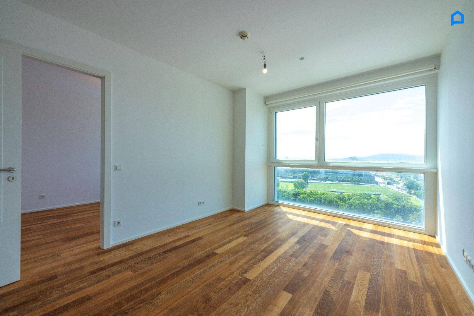 Geräumiges Zimmer mit Holzboden und großen Fenstern, die viel Tageslicht hereinlassen.