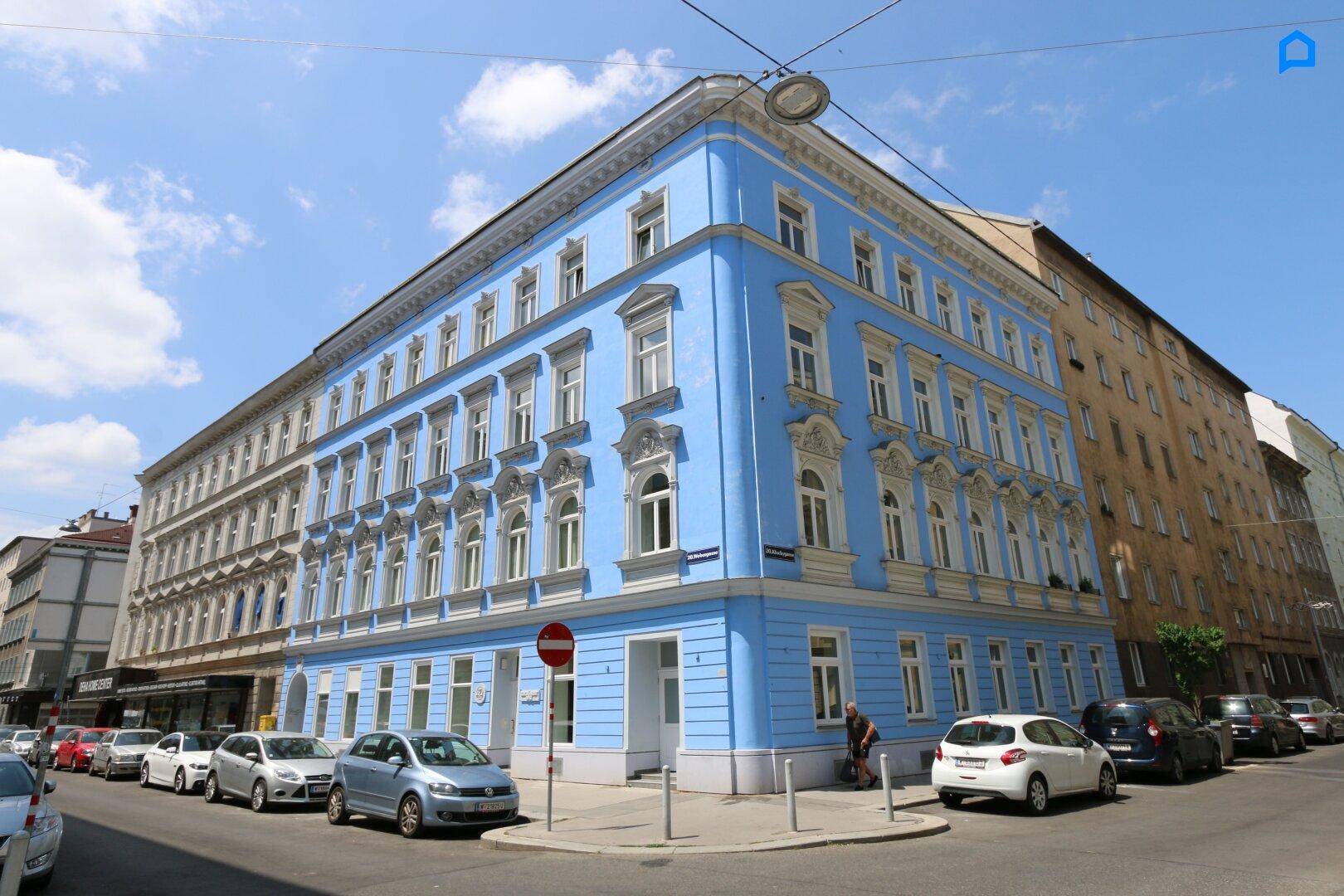 Historisches Eckgebäude mit leuchtend blauer Fassade und reich verzierten Fenstern an einer belebten Stadtstraße.