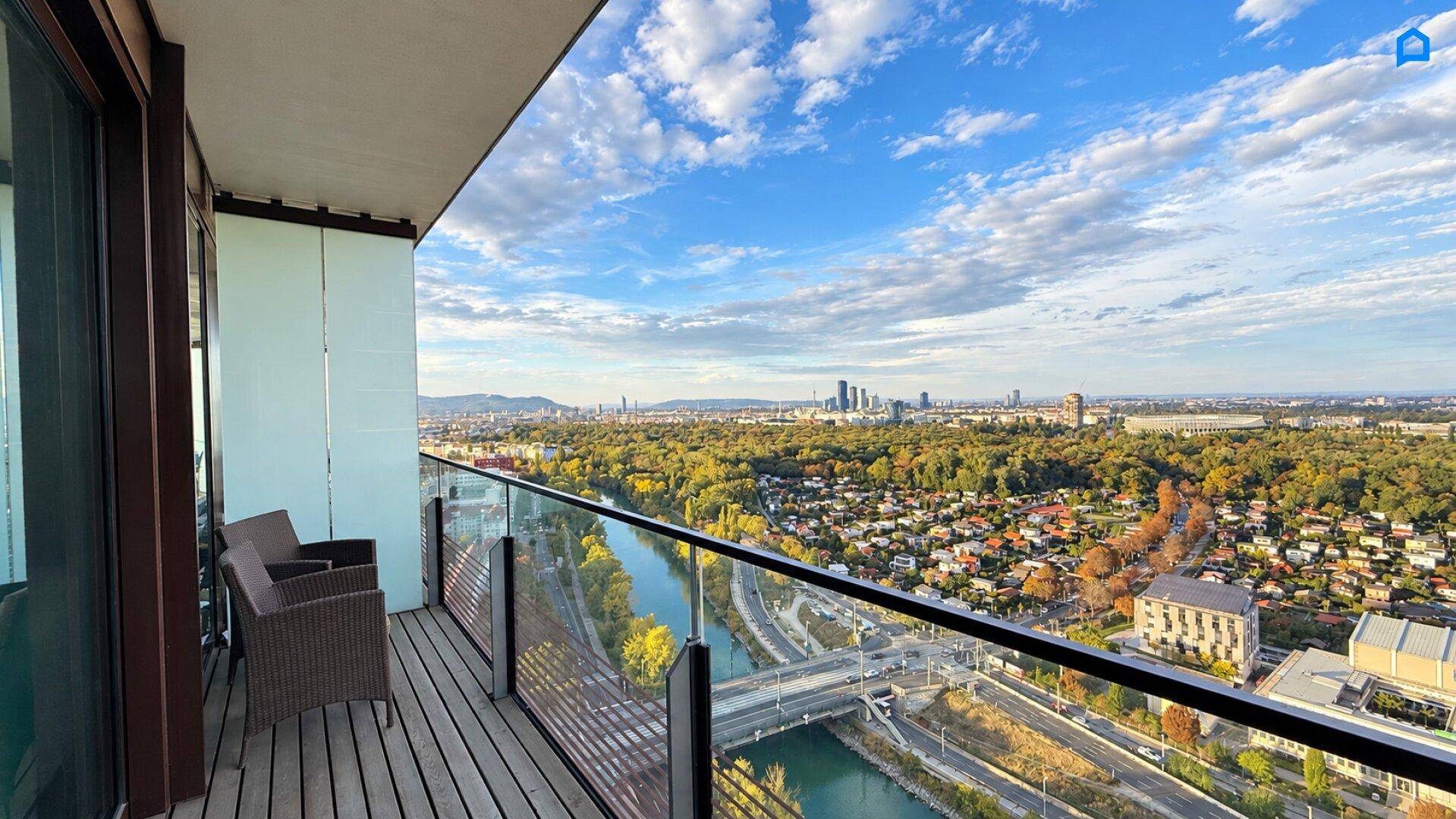 Geräumiger Balkon mit Holzboden, Sitzgelegenheiten und weitem Blick auf Stadt und Fluss.