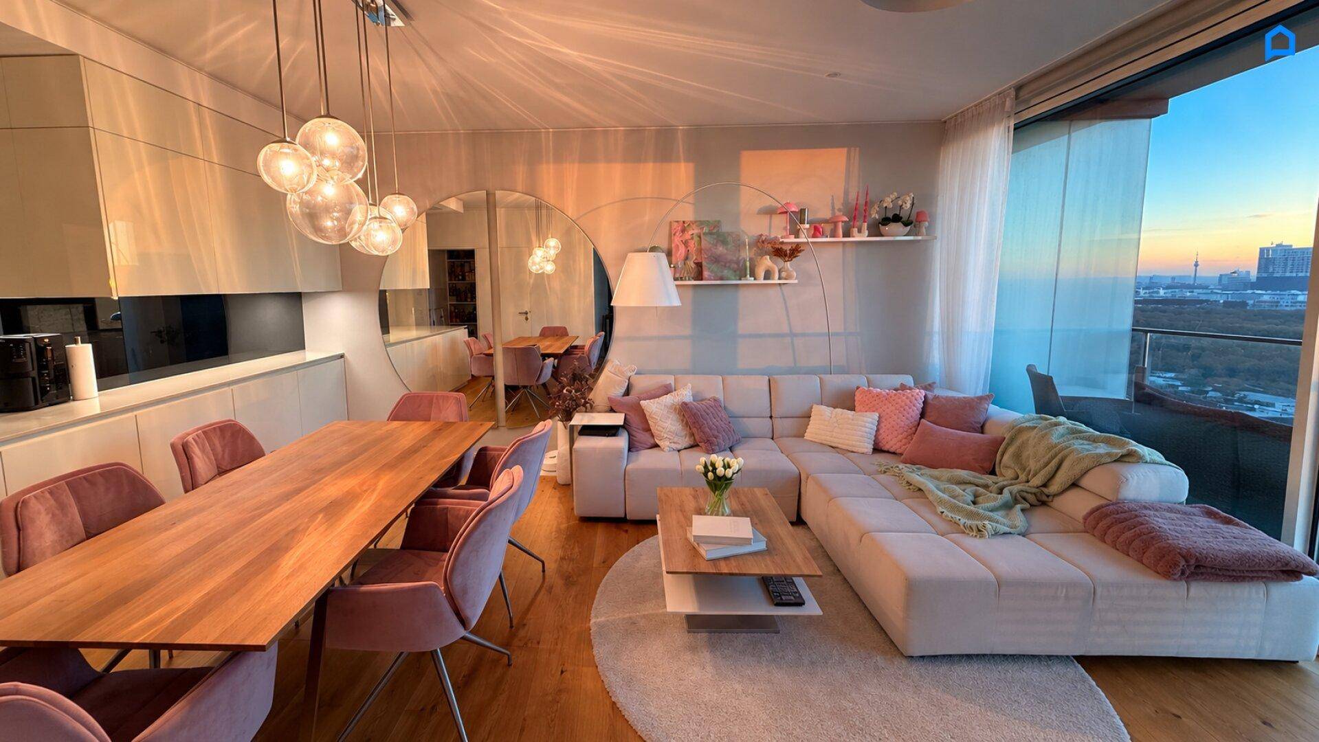 Stilvoller Wohn- und Essbereich mit offener Küche, gemütlichem Sofa und Blick auf die Stadt in der Dämmerung.