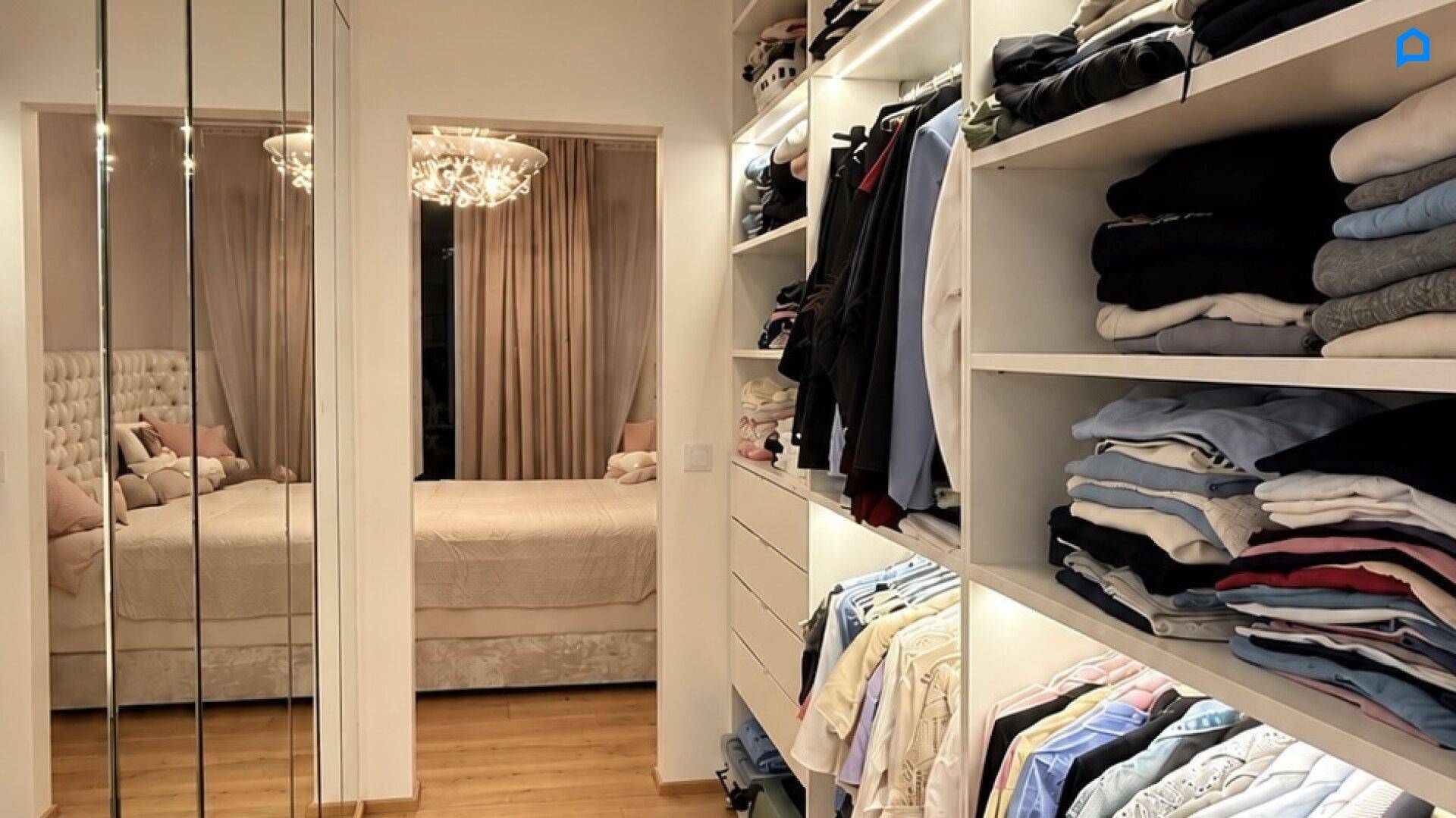 Begehbarer Kleiderschrank mit Regalen und Spiegeltüren, mit Blick auf das angrenzende Schlafzimmer.