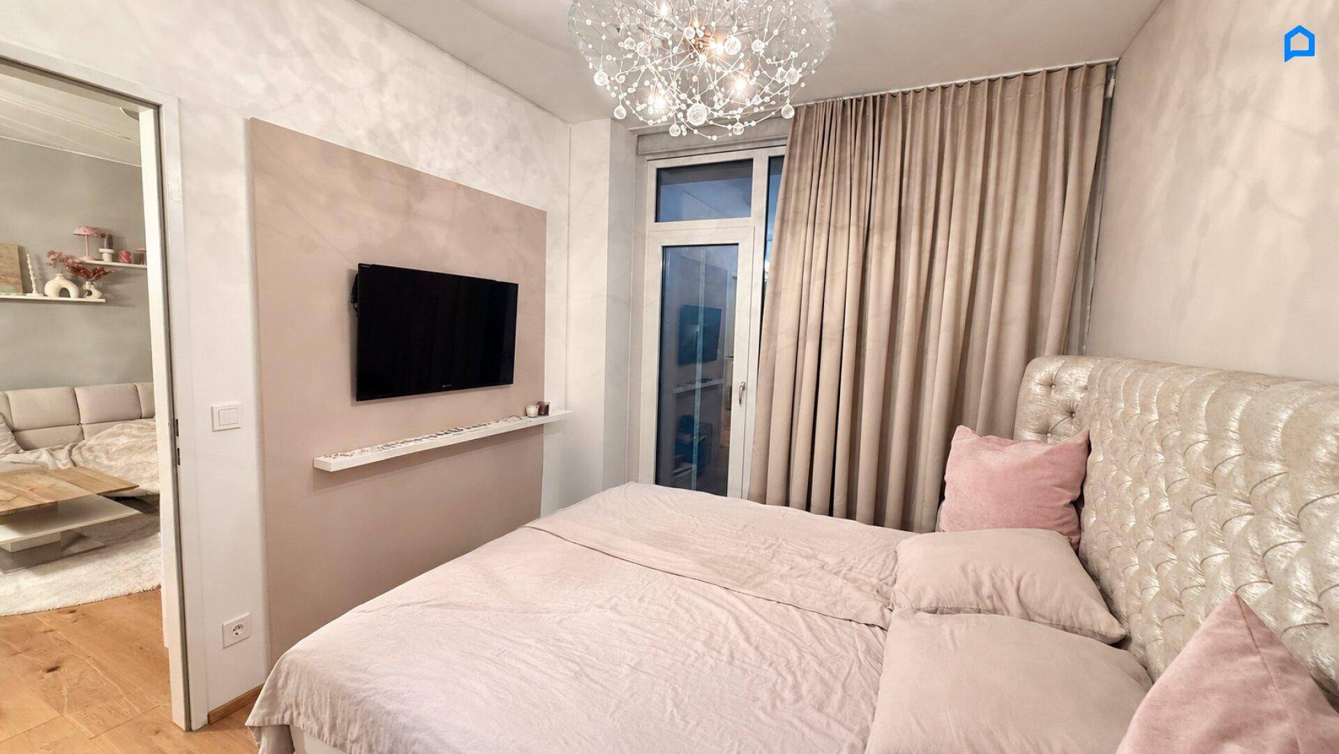 Elegantes Schlafzimmer mit großem Bett, Wandfernseher und Zugang zum angrenzenden Wohnbereich.