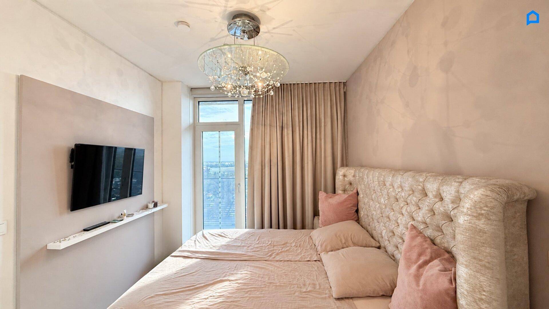 Helles Schlafzimmer mit großem Bett, Wandfernseher und raumhohen Fenstern mit Stadtblick.