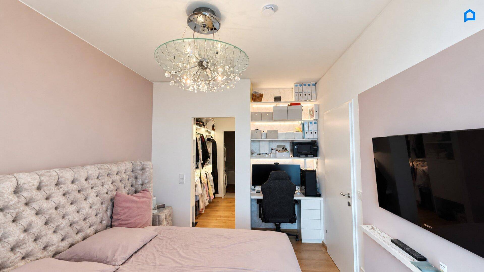 Schlafzimmer mit großem Bett, integriertem Arbeitsbereich und direktem Zugang zum begehbaren Kleiderschrank.