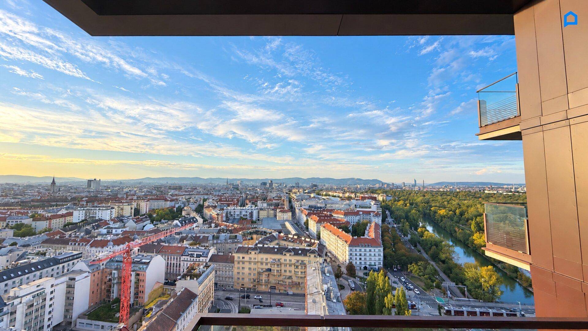 Panoramablick über die Stadt Wien mit Fluss und Bergen im Hintergrund bei Sonnenuntergang.