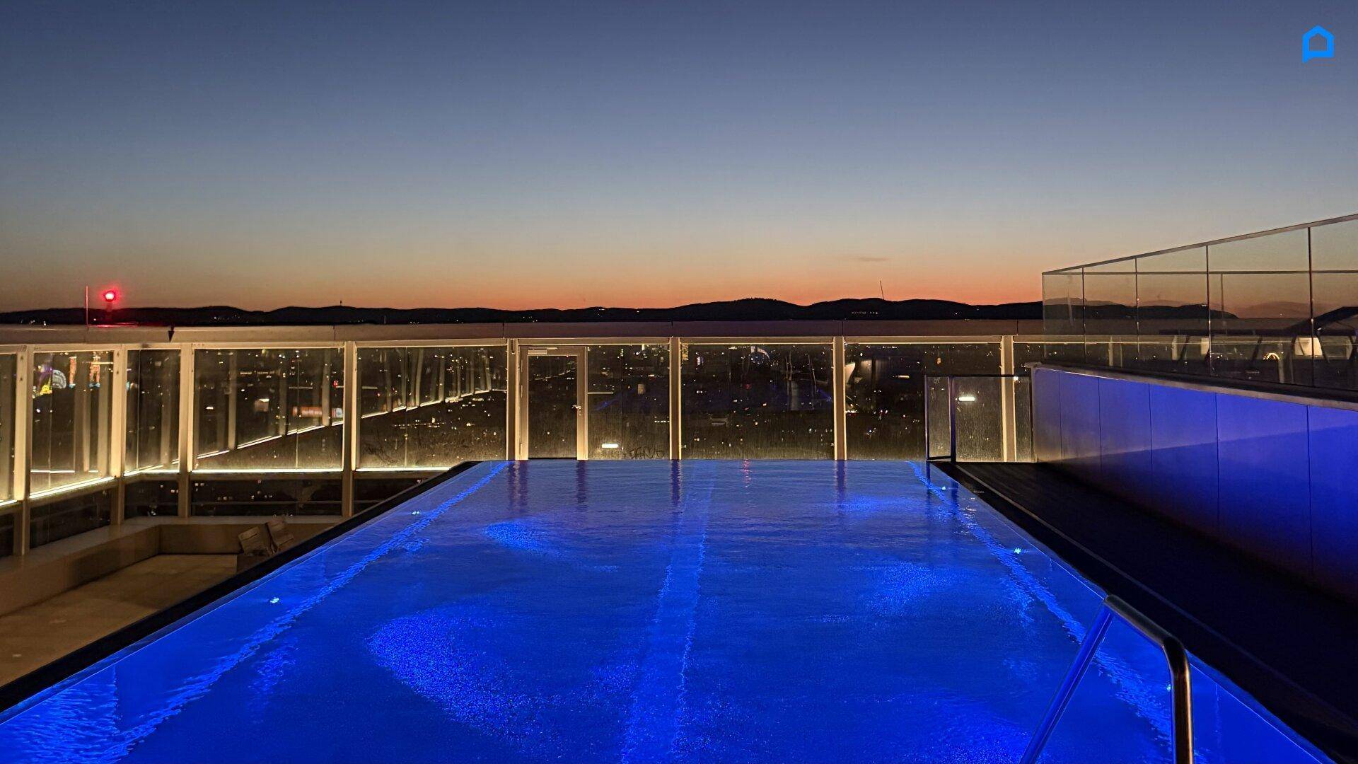 Beeindruckender Infinity-Pool auf dem Dach mit nächtlichem Panoramablick über die beleuchtete Stadt.