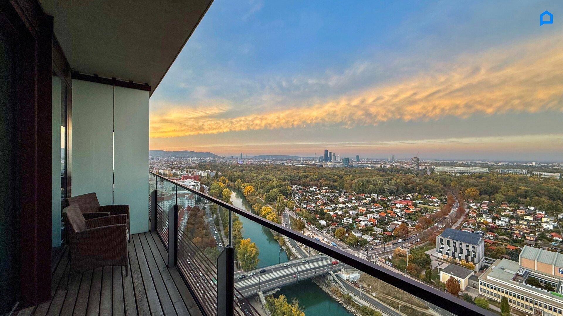 Balkon mit Holzboden und atemberaubendem Panoramablick auf die Stadt und den Fluss bei Sonnenuntergang.