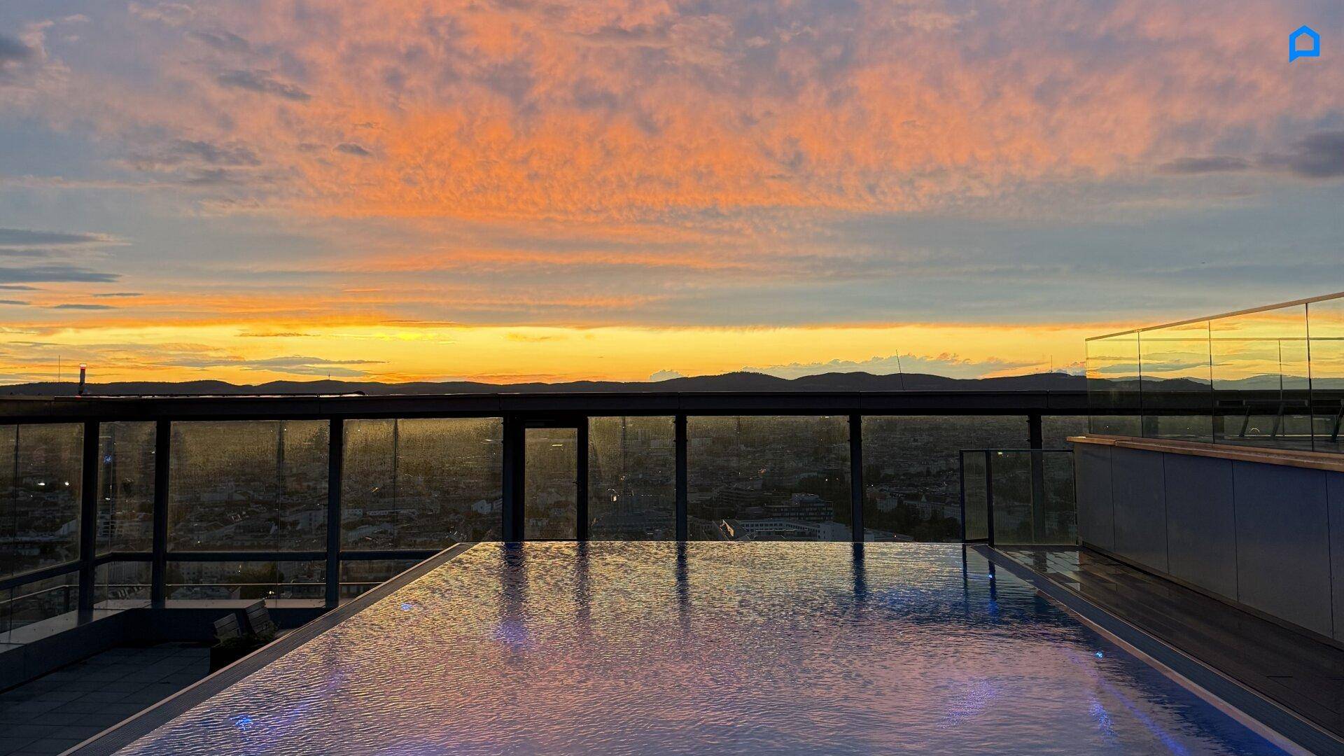 Infinity-Pool auf dem Dach mit spektakulärem Sonnenuntergang über der Stadt.