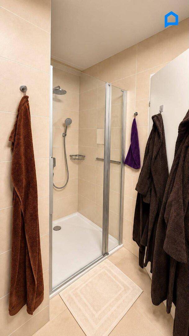 Moderne Duschkabine mit Glasabtrennung und beigefarbenen Fliesen im Badezimmer.