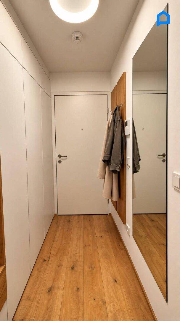 Langer Flur mit Holzboden, großem Spiegel und Garderobe, der zu den weiteren Räumen führt.