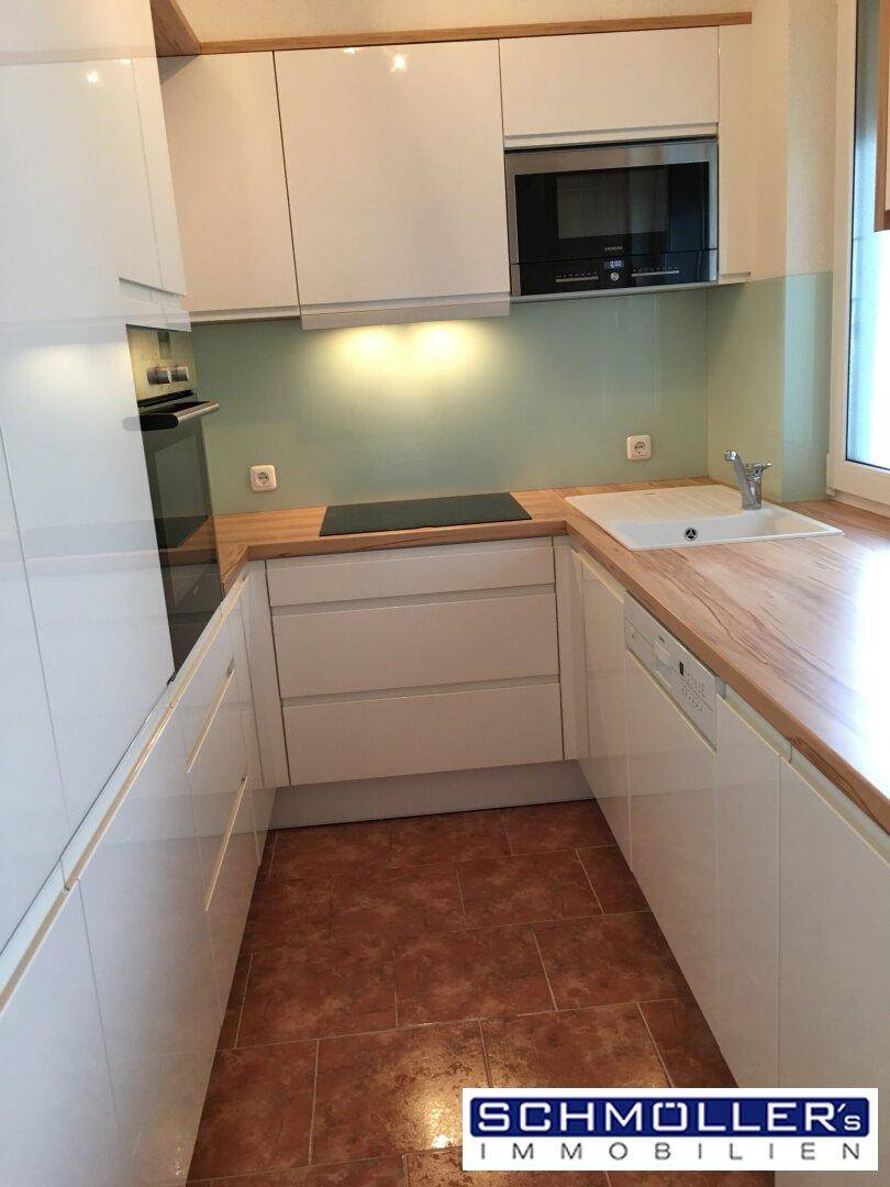 Moderne Küche mit weißen Schränken, Holzarbeitsplatte und integrierten Geräten.